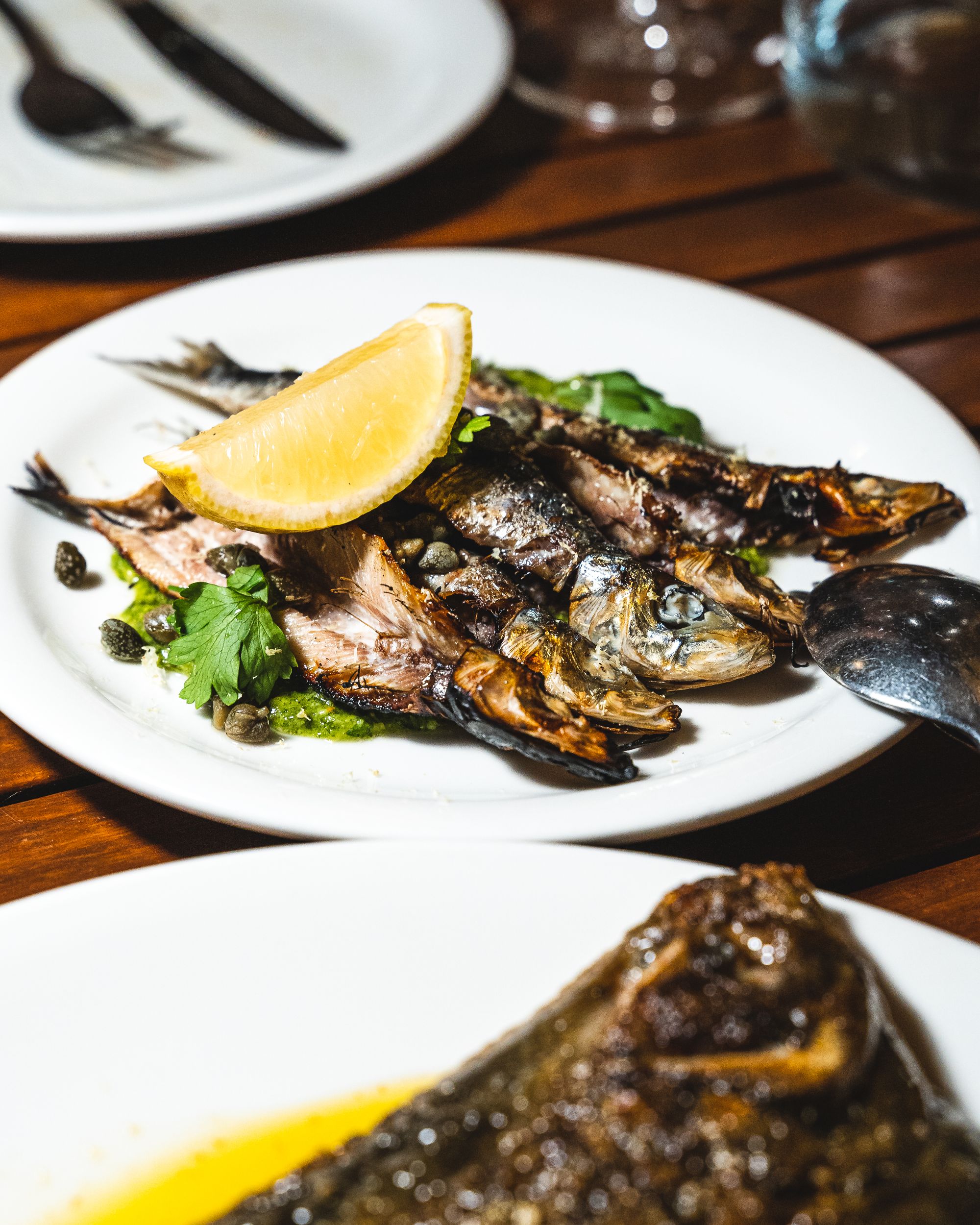 Close up of sardines on a plate, garnished with a lemon wedge and greens