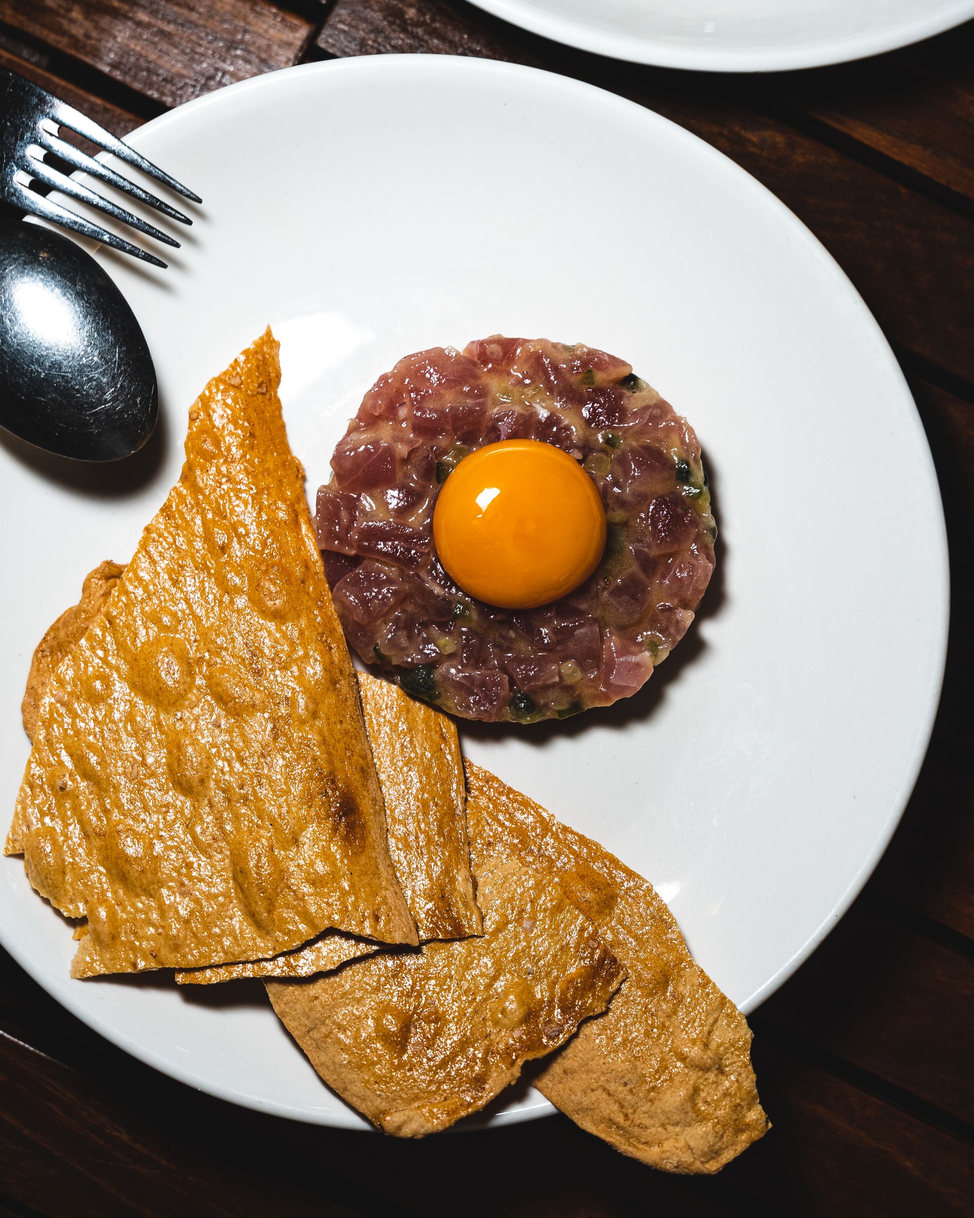 Raw tuna shaped in a circle with an egg yolk on top with crisps served on the side