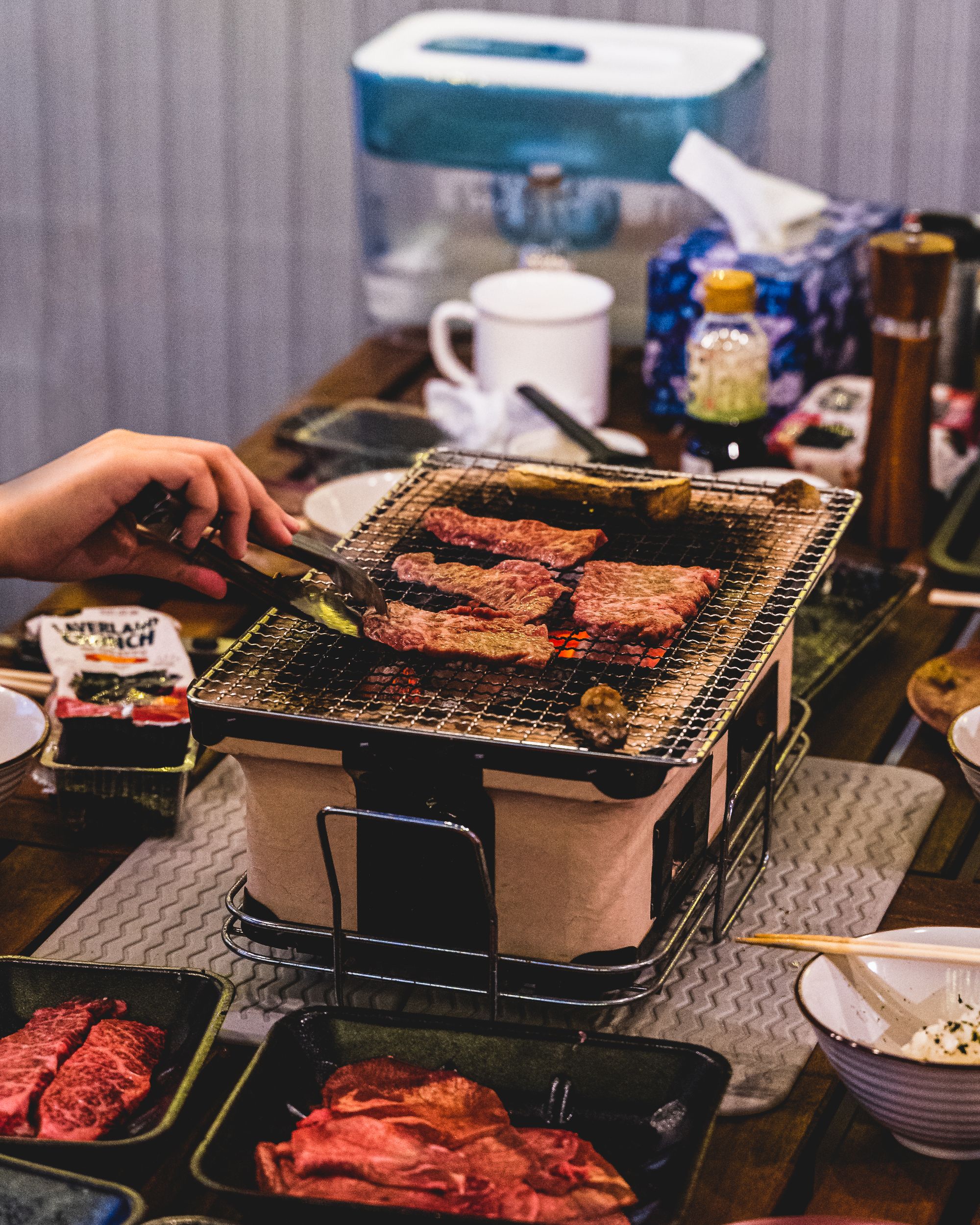 A hand using tongs to flip meat which is cooking on a mesh over charcoal