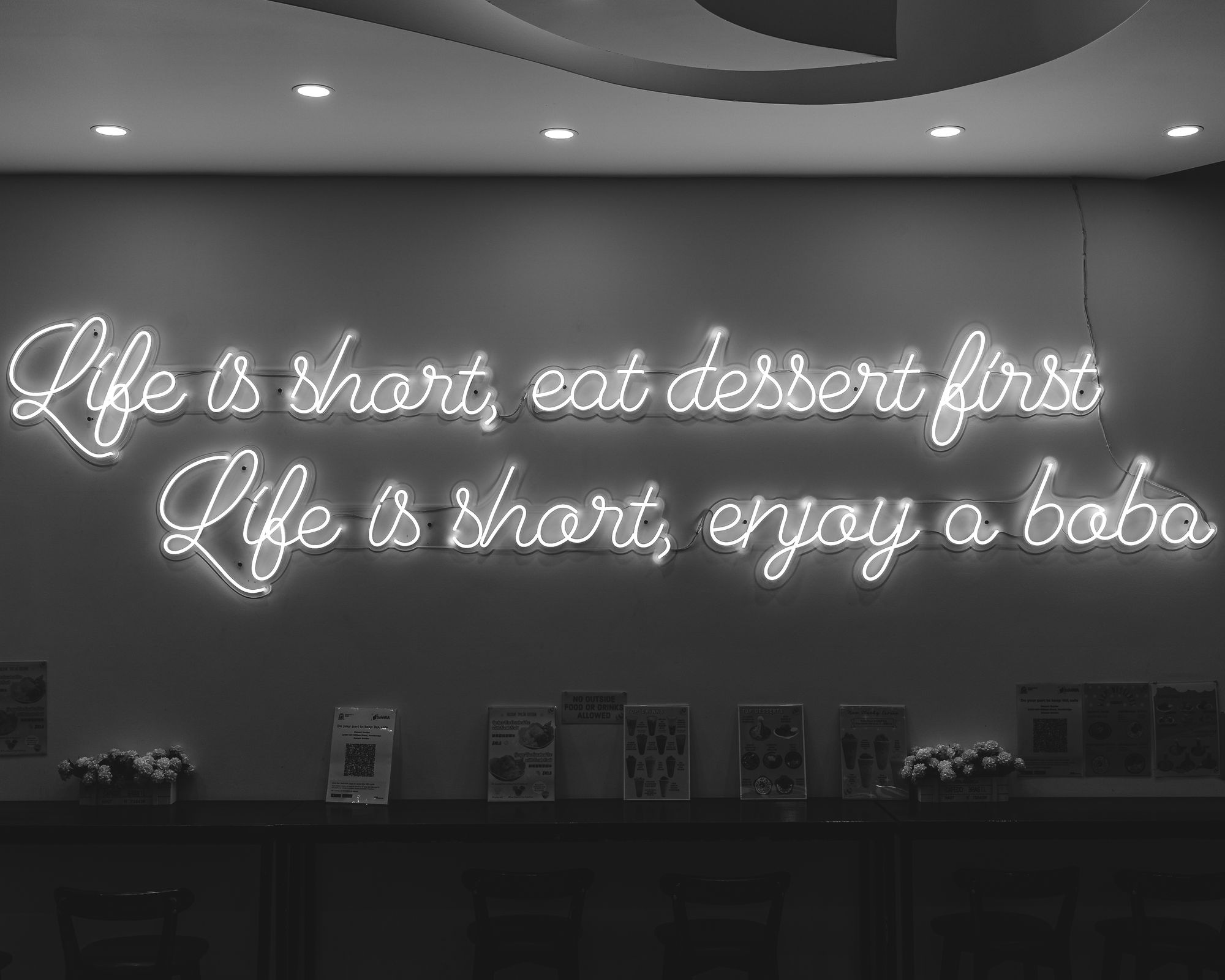 Black and white photo with a sign saying "life is short, eat dessert first.Life is short, enjoy a boba"