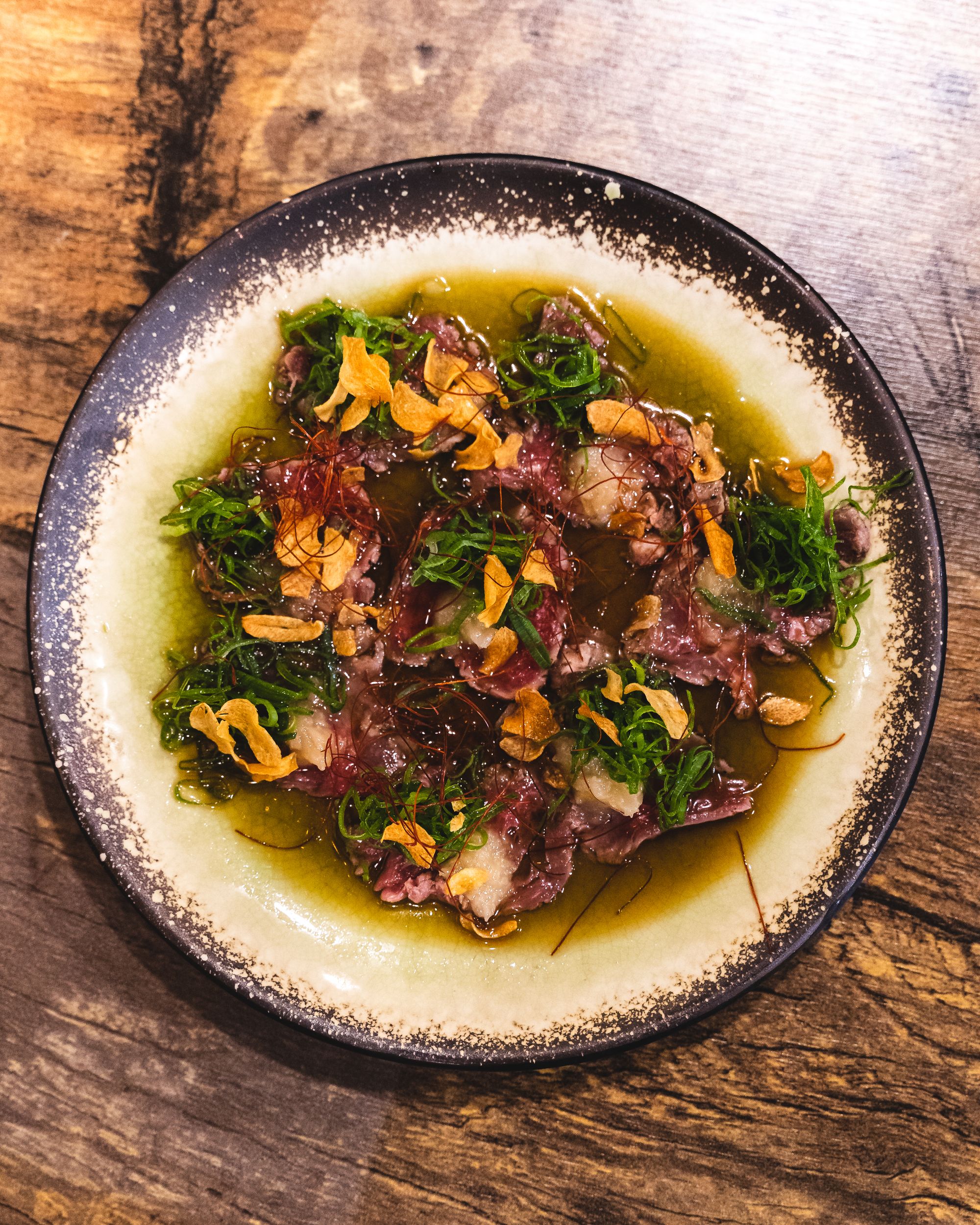 An overhead shot of raw beef tataiki, spring onion, garlic chips and soy sauce