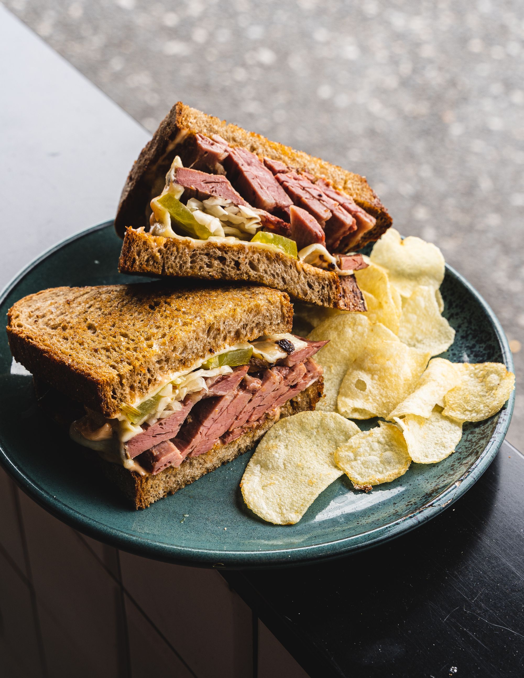 Close up shot of reuben sandwich stacked on-top of each other, with a side of crisps