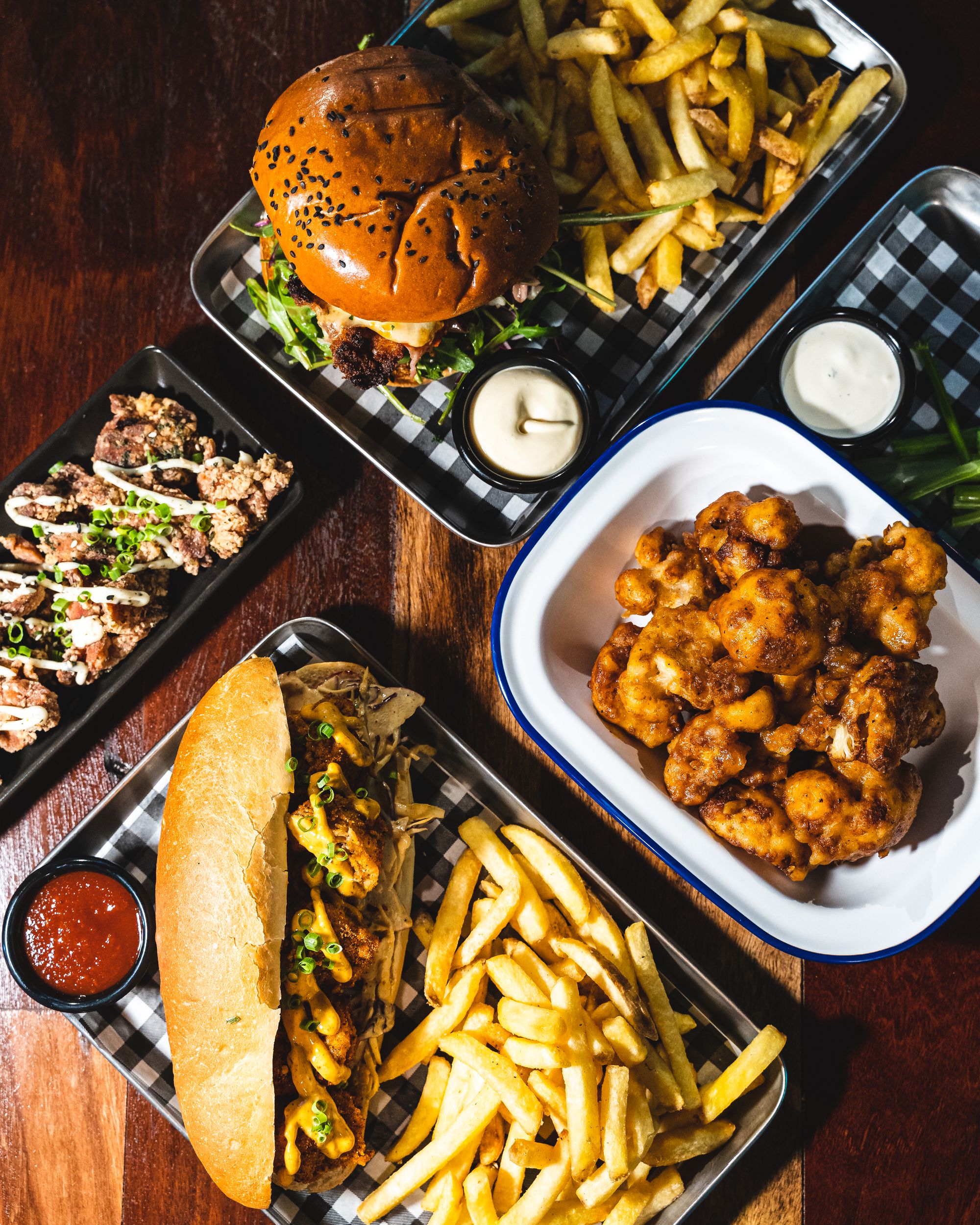 A flat lay of a burger, fried cauliflower, po-boy and fried chicken