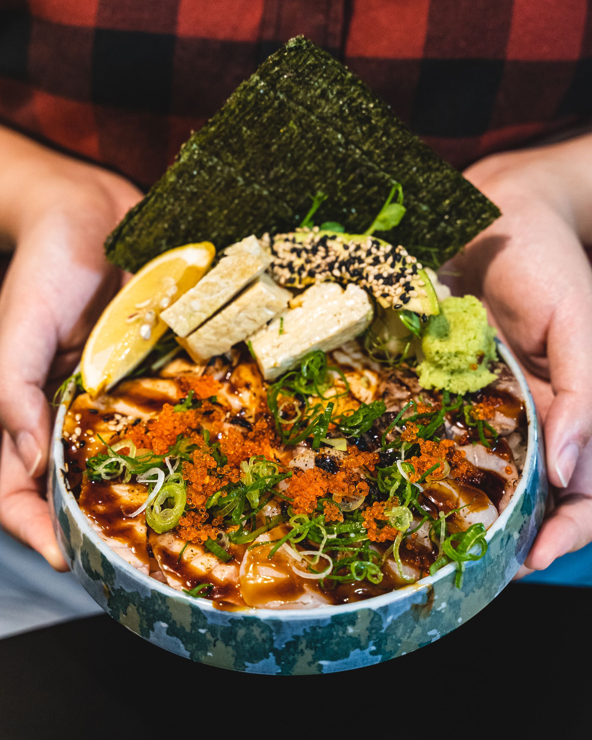 Close up of hands holding a bowl with aburi seared sashimi topped with fish roe