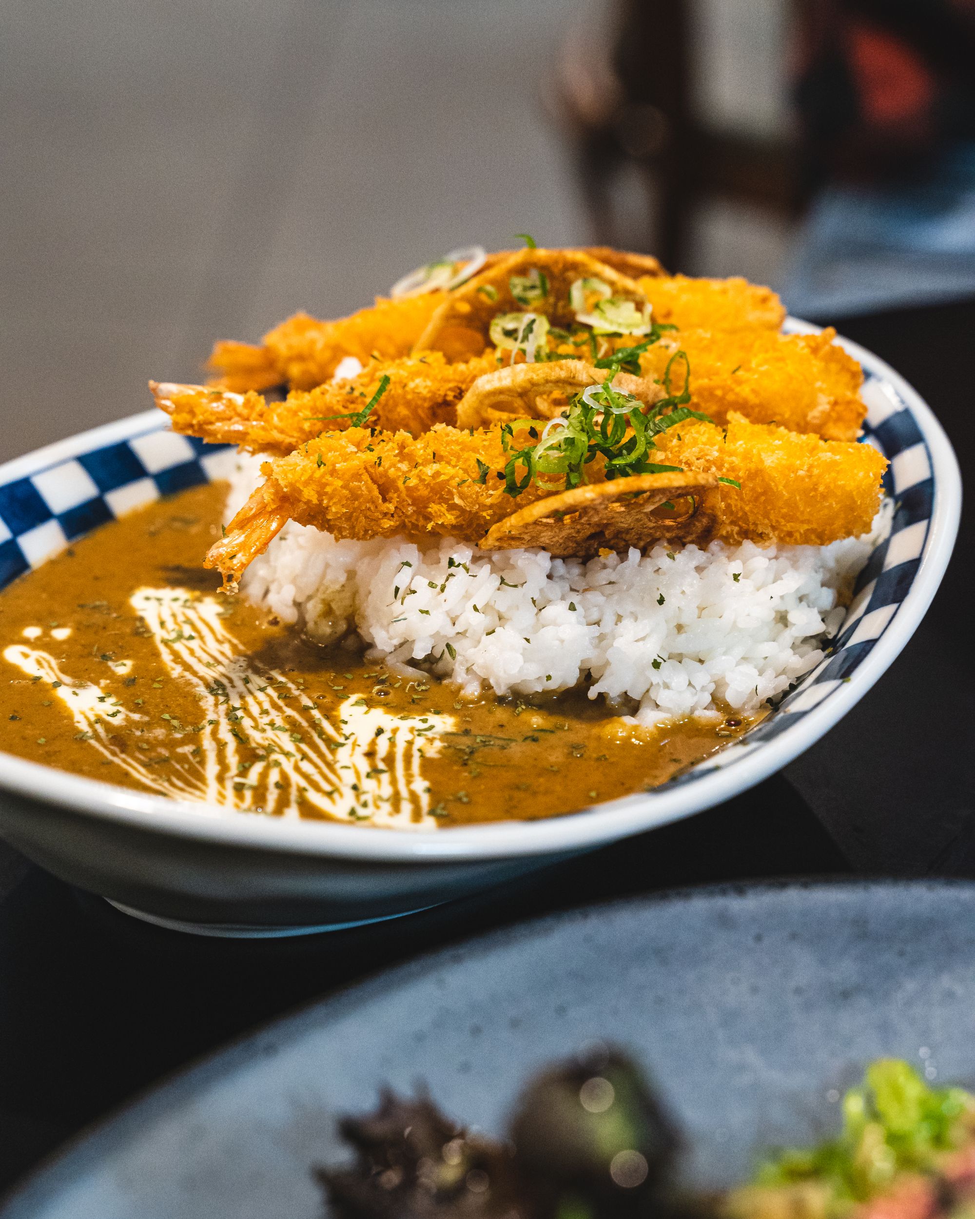 A bowl of Japanese curry, with the sauce on the left, rice on the right and three fried prawns on-top of the rice