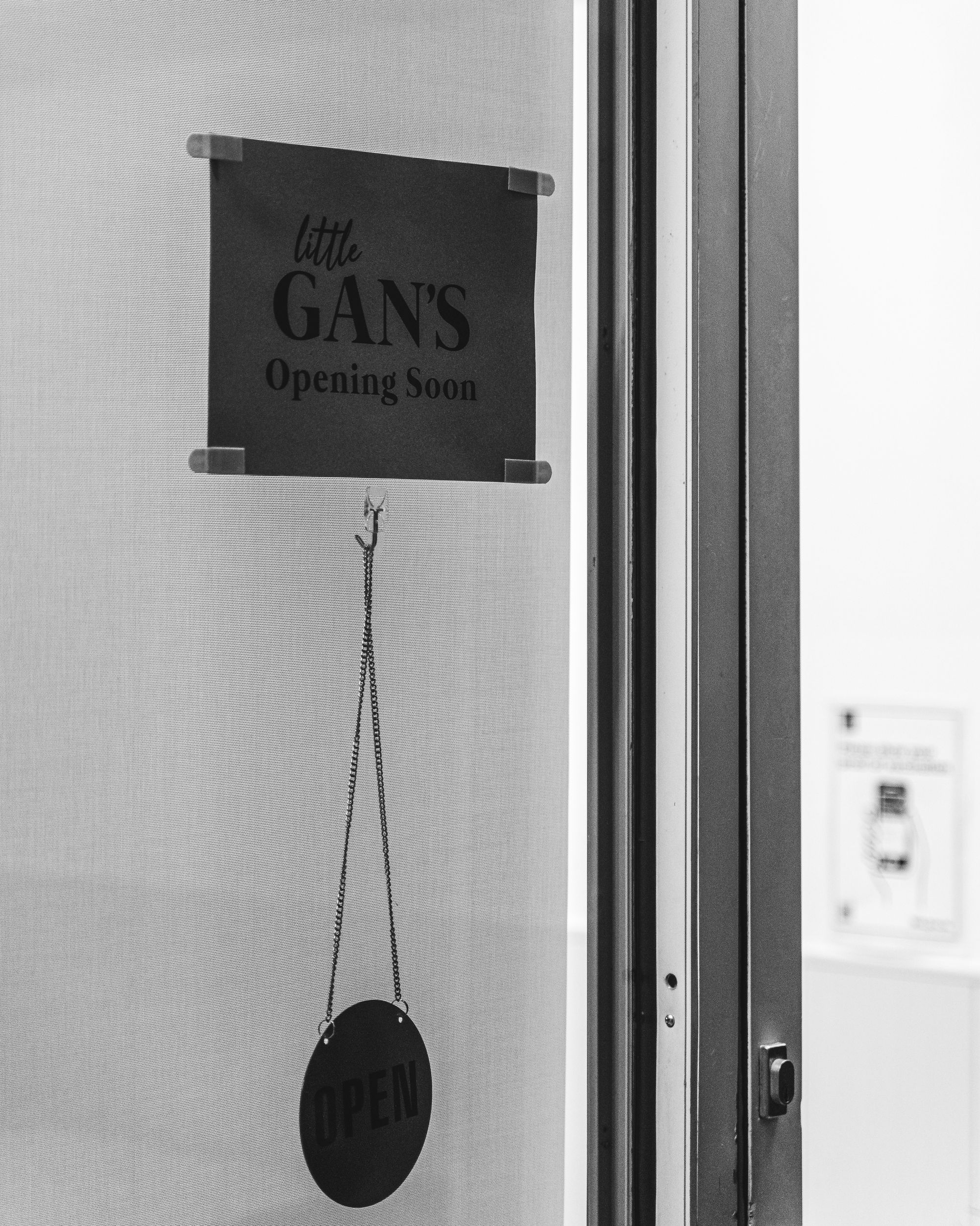 Black and white image showing a open sign with "little Gan's" on it