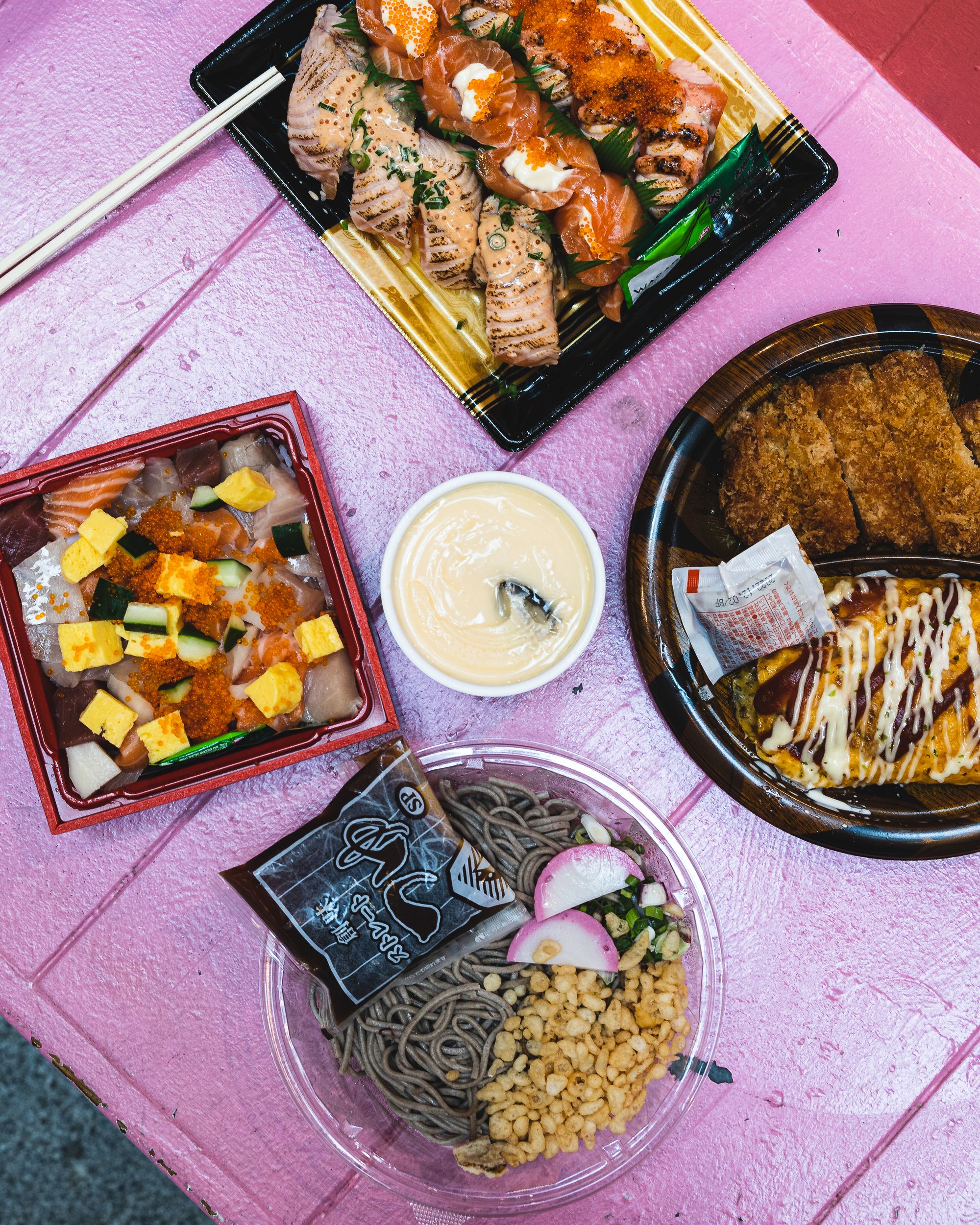 A spread of Japanese food on a pink bench