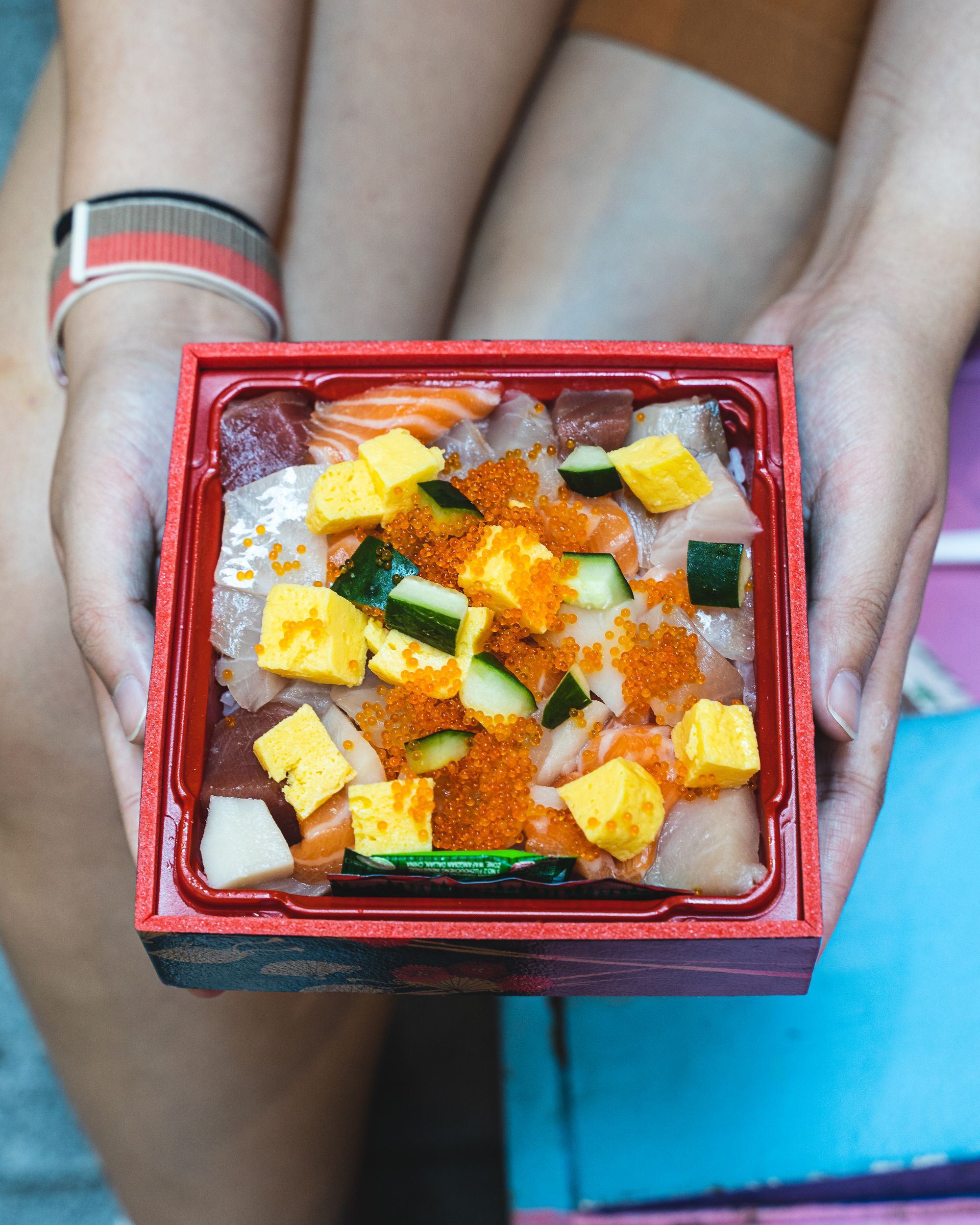 A hand holding a bento box fulled of colourful sashimi cut into cubes