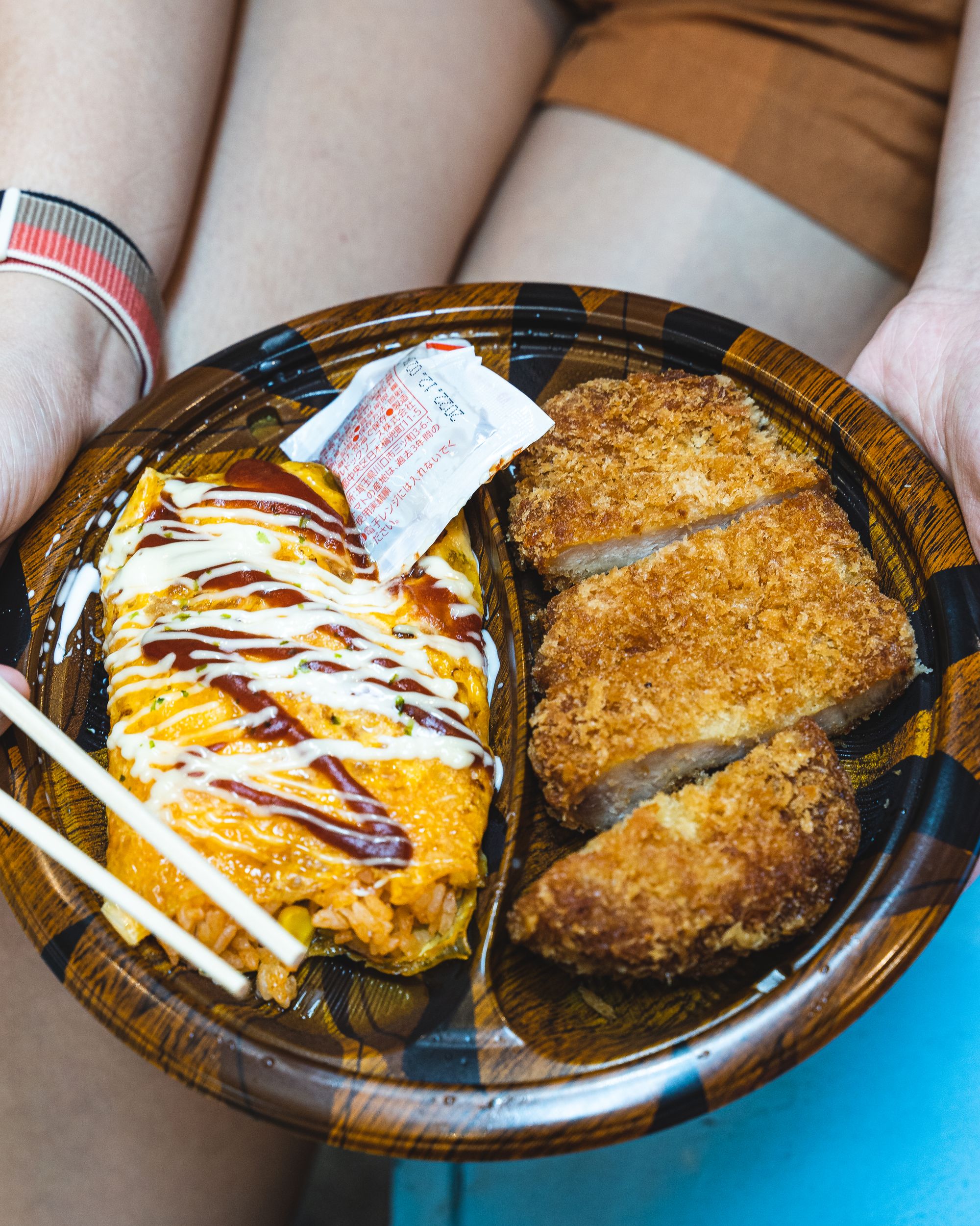 A hand holding a plate of omurice with a fried pork cutlet on the side