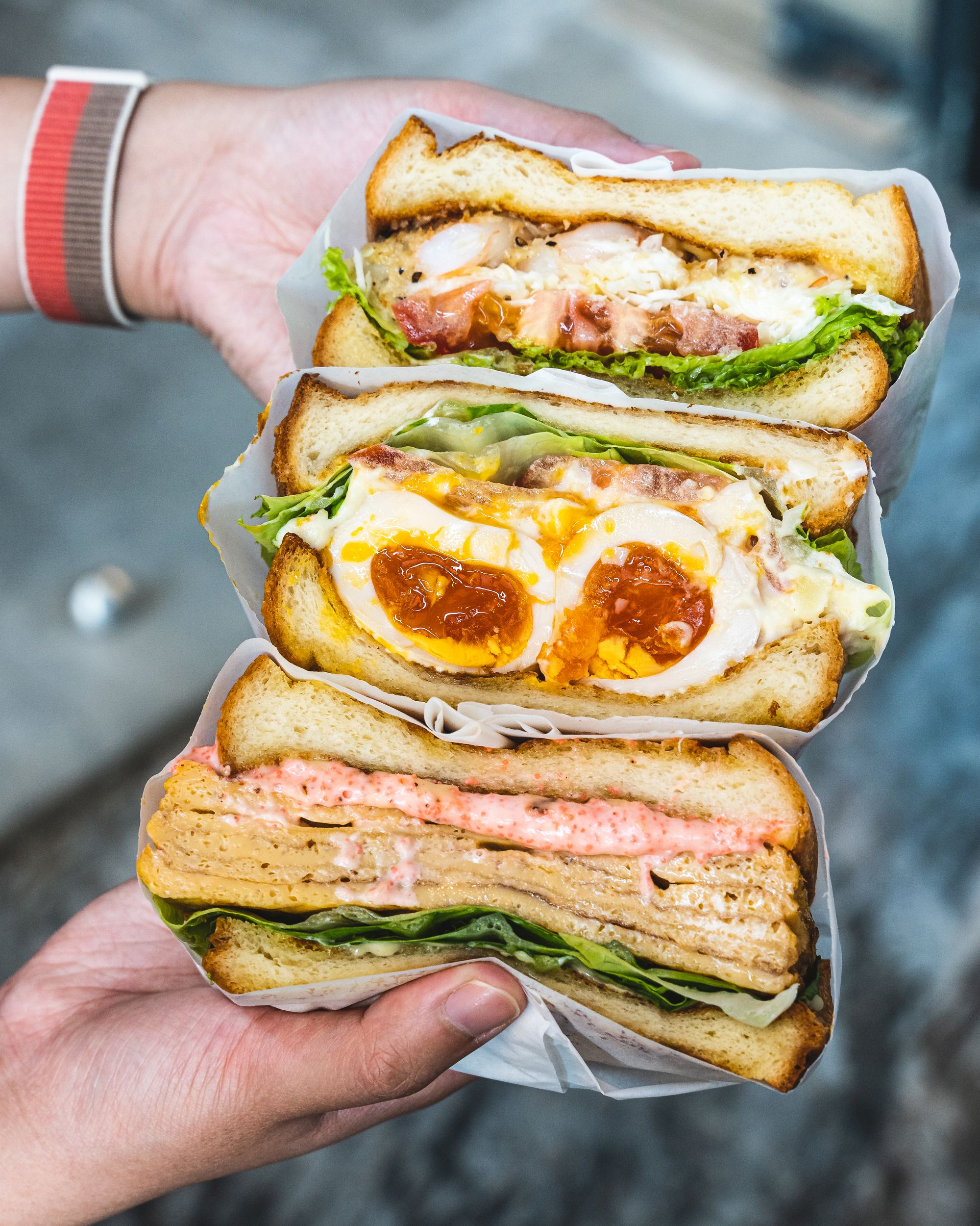 A hand holding a stack of sandwiches which are popping with fillings