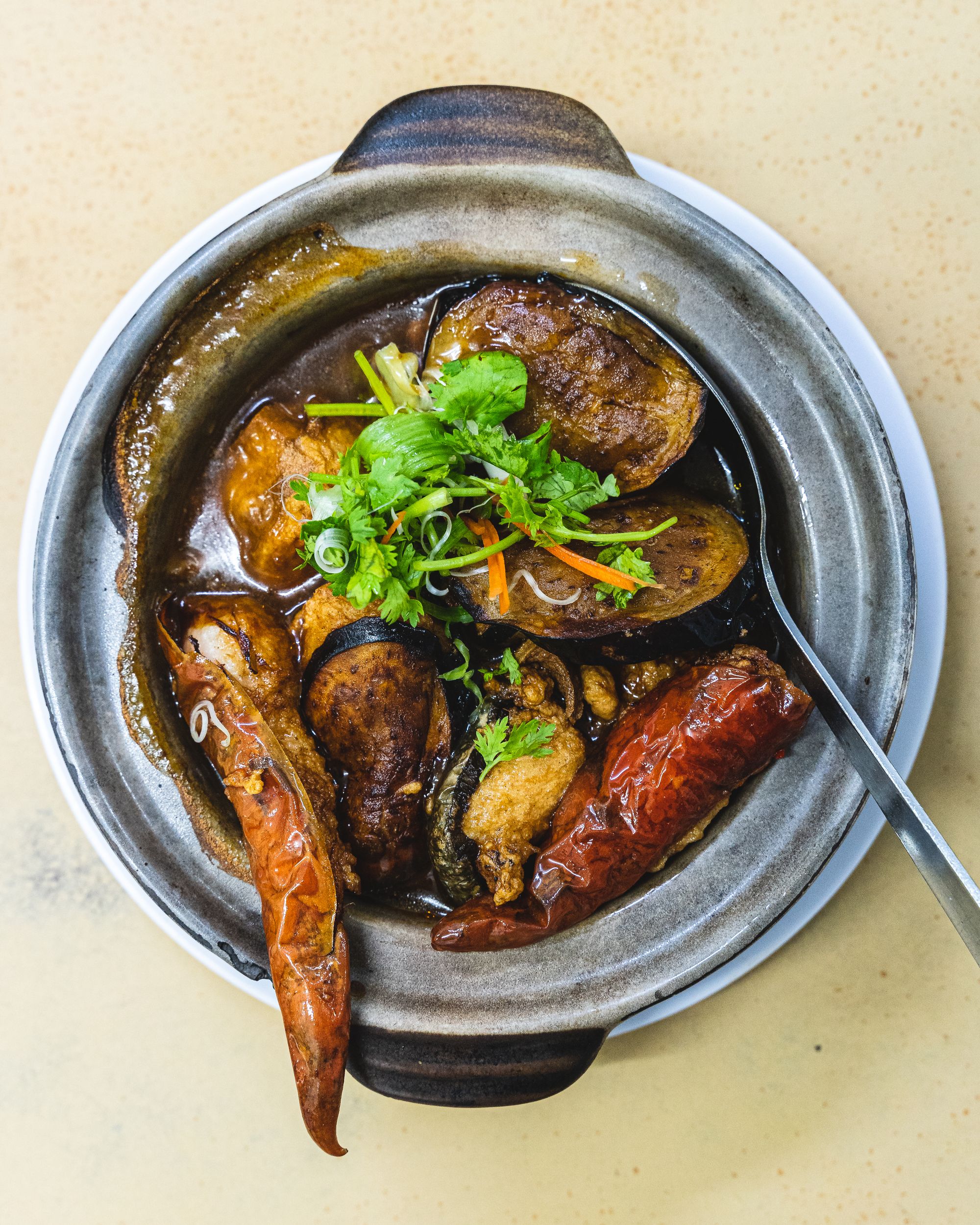 Close up shot of a claypot with eggplant, tofu and green garnish