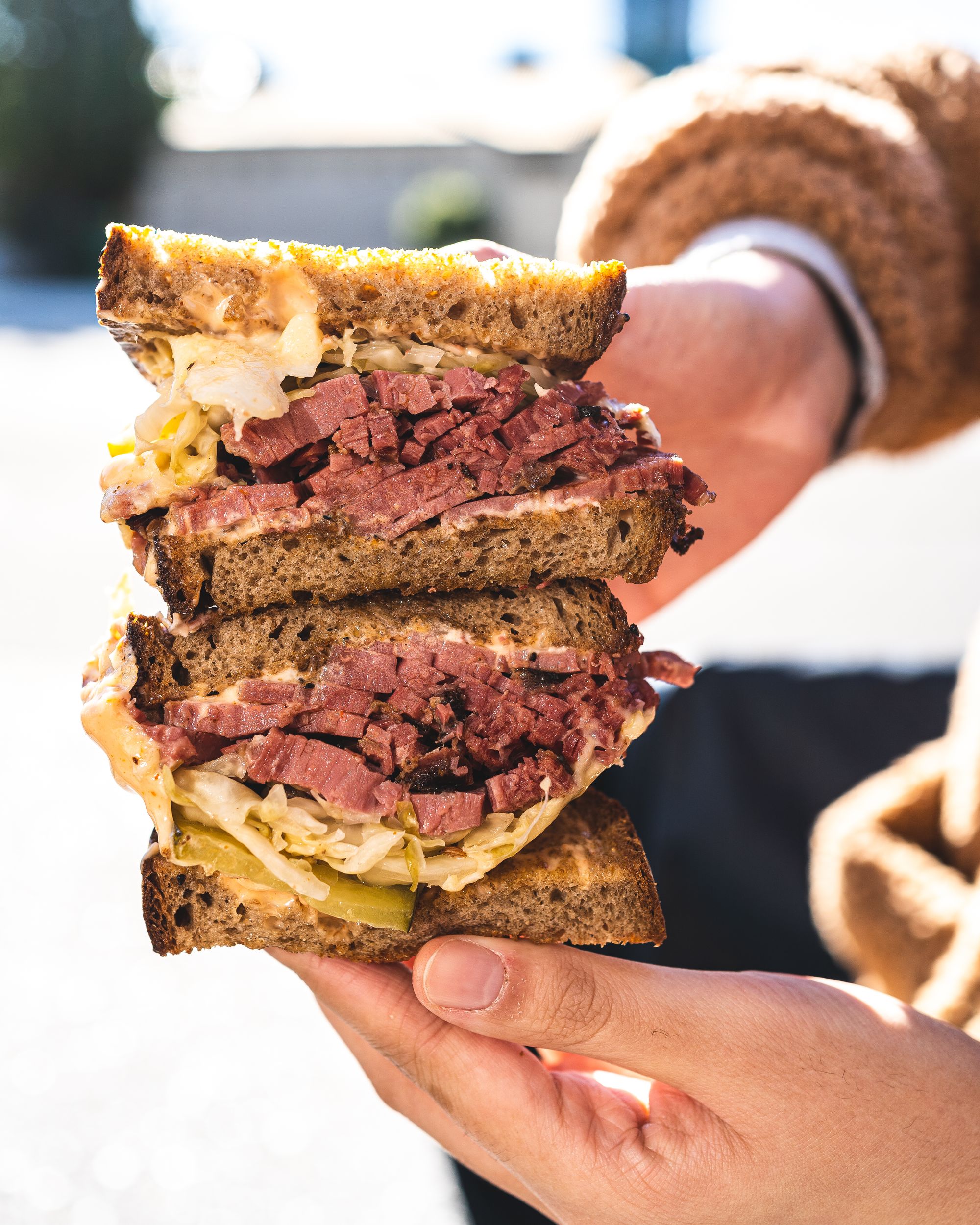 Close up shot of reuben sandwich being stacked on-top of each other and held between hands, showing cuts of pastrami