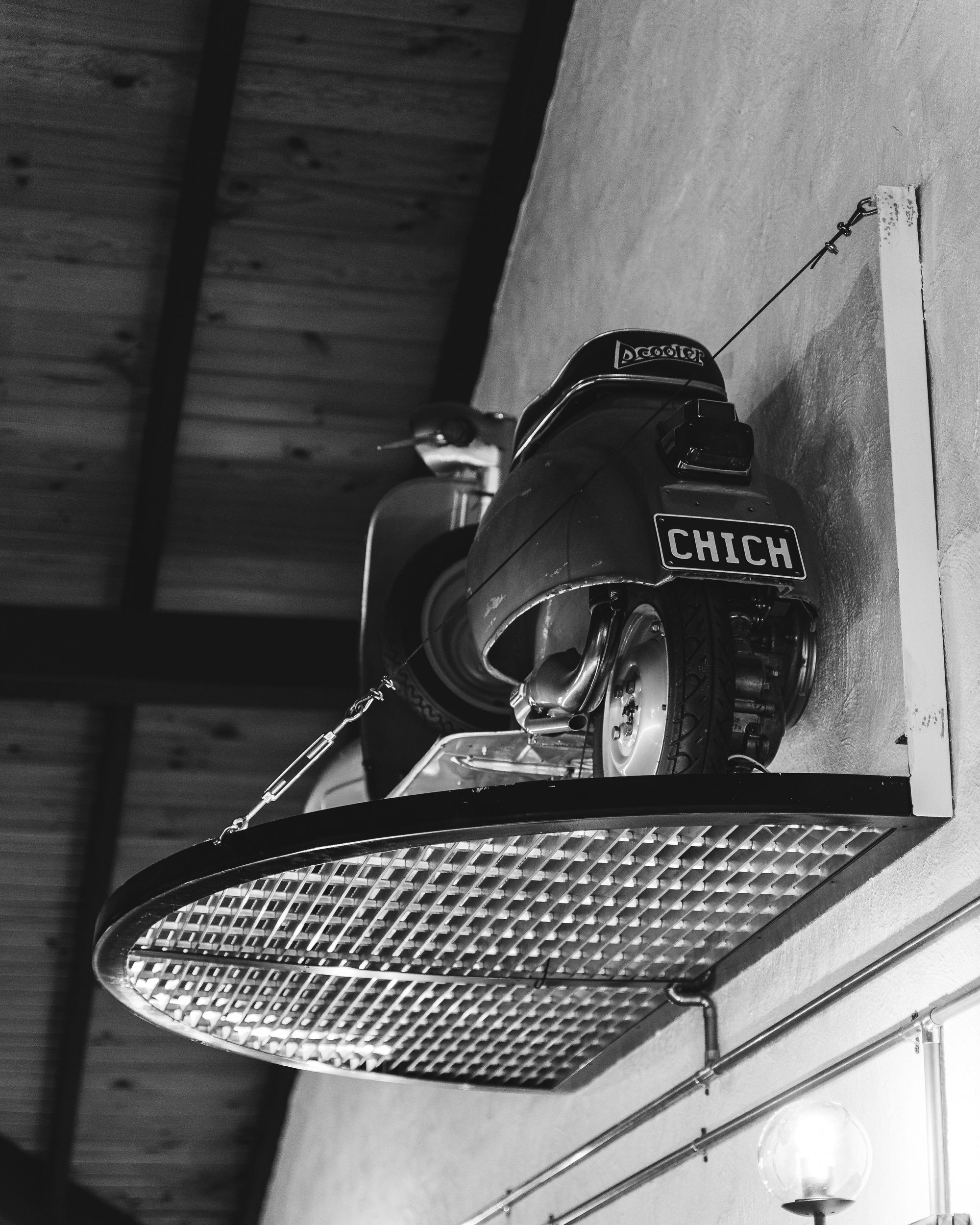 Black and white shot of a 1963 Vespa scooter on a metal shelf with the licence plate "CHICH"