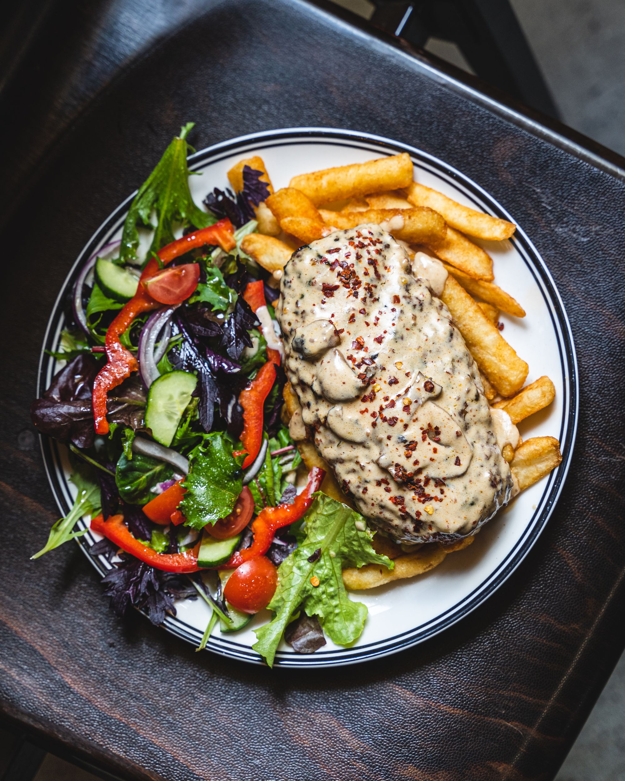 Close up view of a oval shaped beef patty with mushroom looking sauce, sitting on-top of chips and a salad