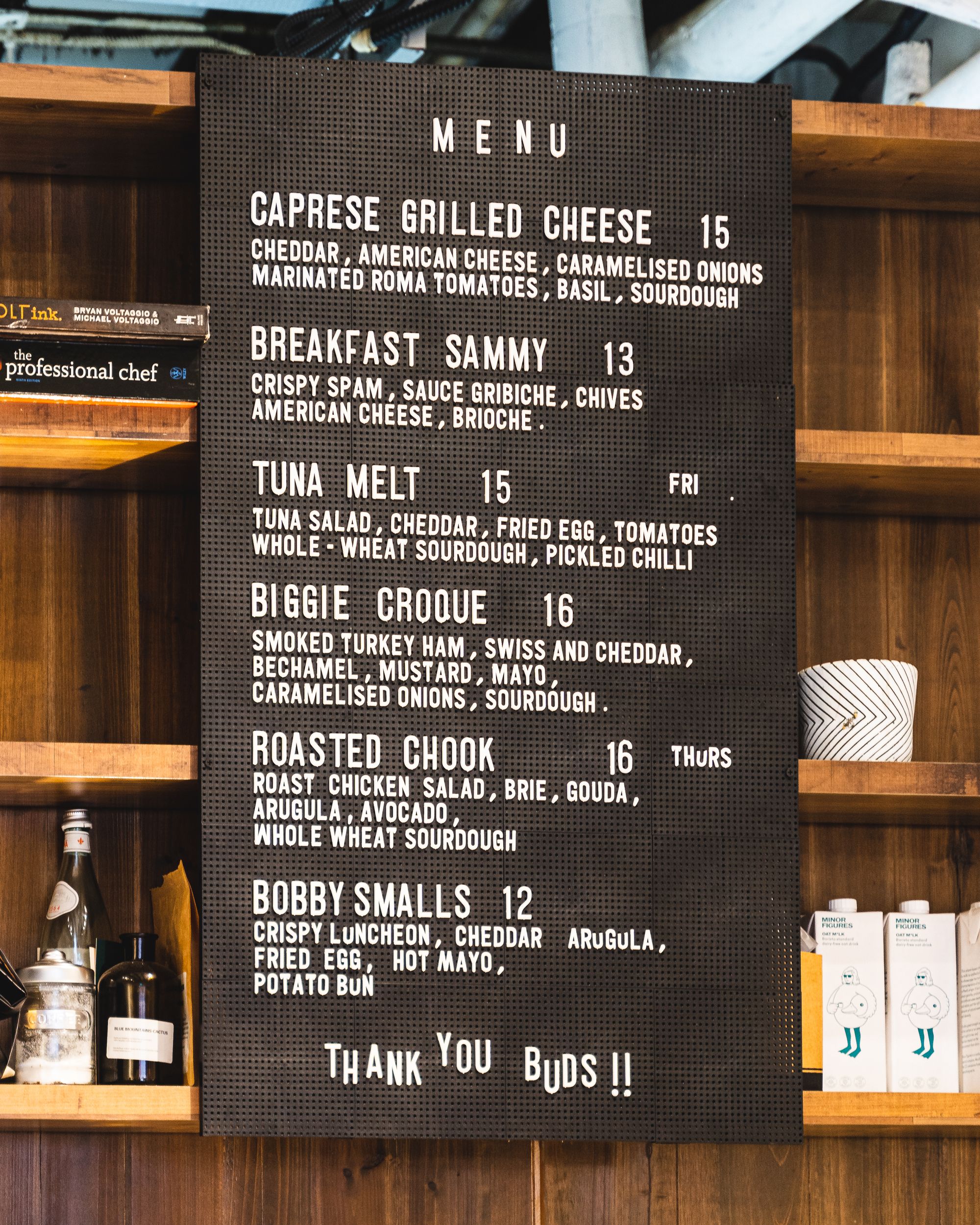 A photo of a cafe menu hung on the wall in-front of wooden shelves