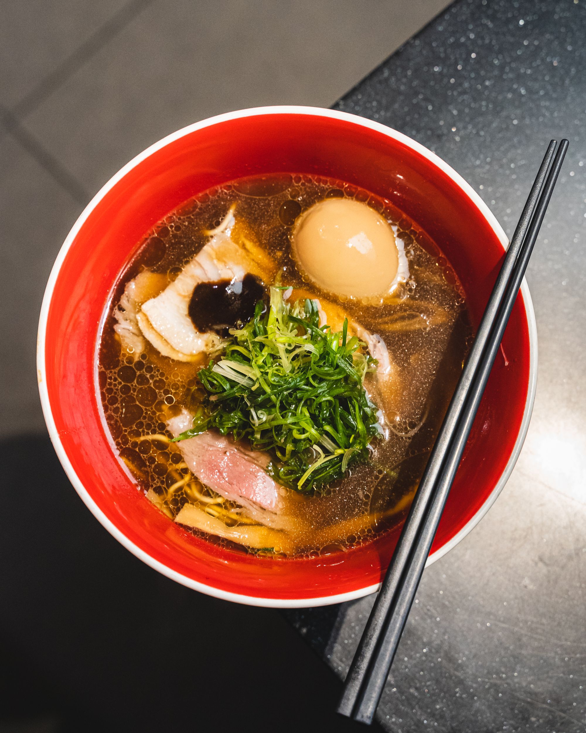 Top down shop of a bowl of soy ramen with egg and a pair of chopsticks rested on-top