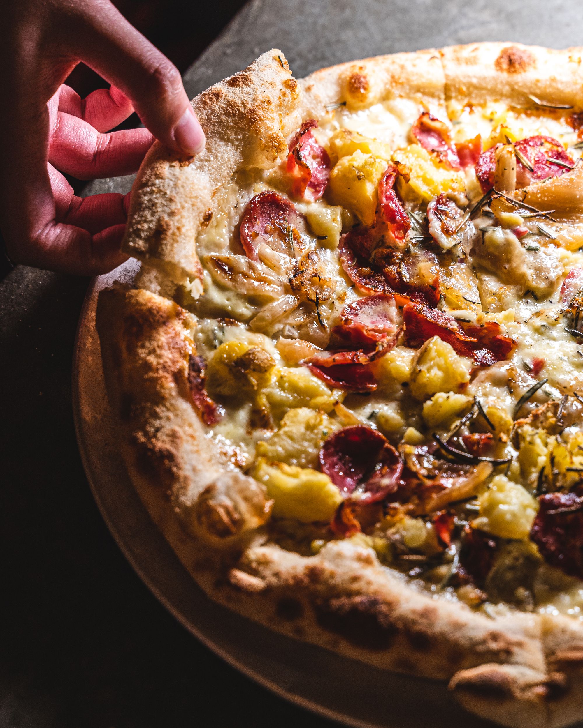 Hand picking up a slice of pizza with pepperoni, cheese and potato