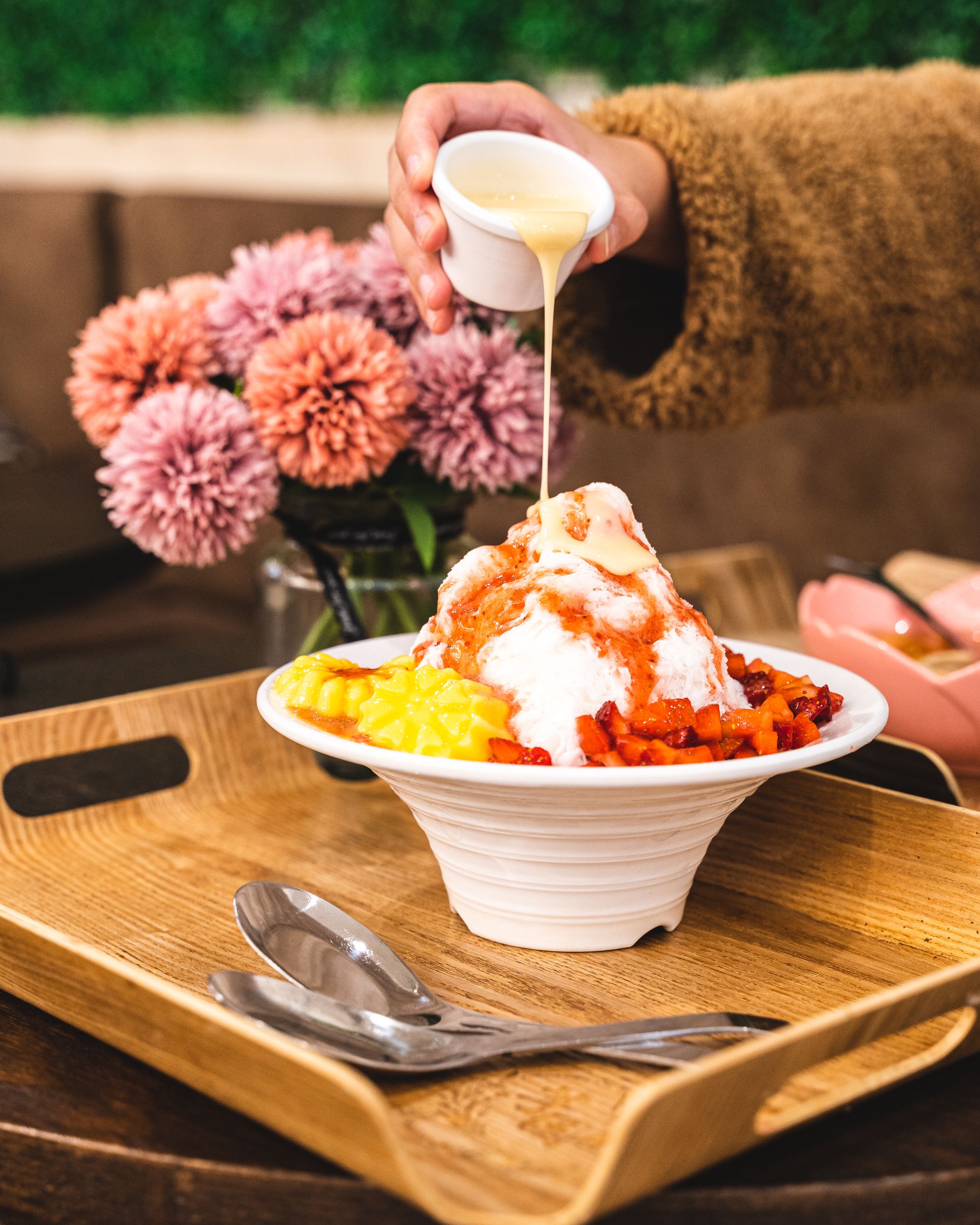 Hand pouring condensed milk from a ramakin ontop of a shaved ice dessert