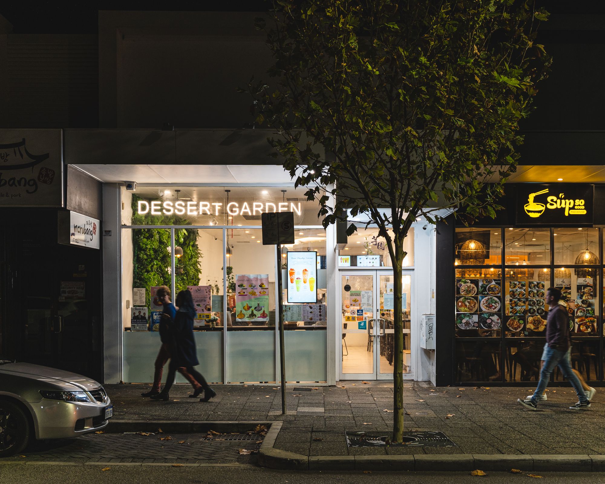 Dimly lit exterior photo of Dessert Garden with people walking past