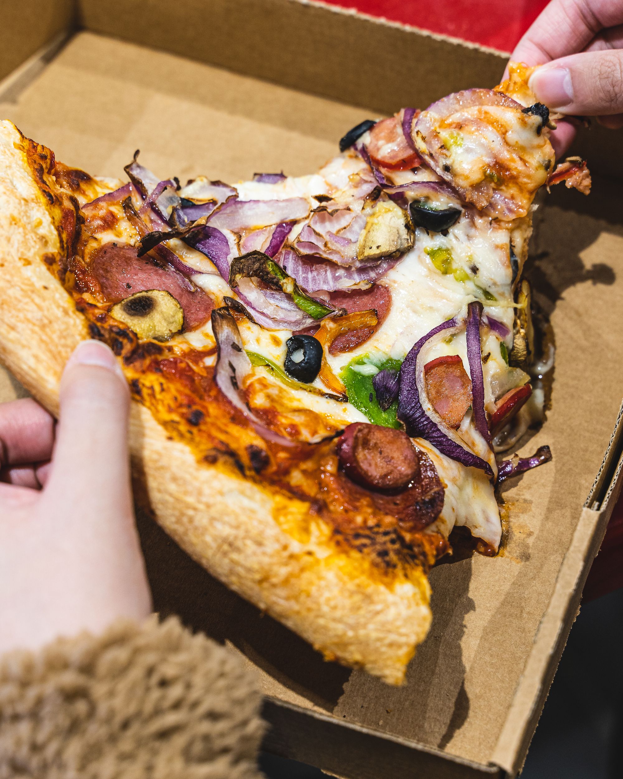 Close up shot of hand holding a slice of supreme pizza