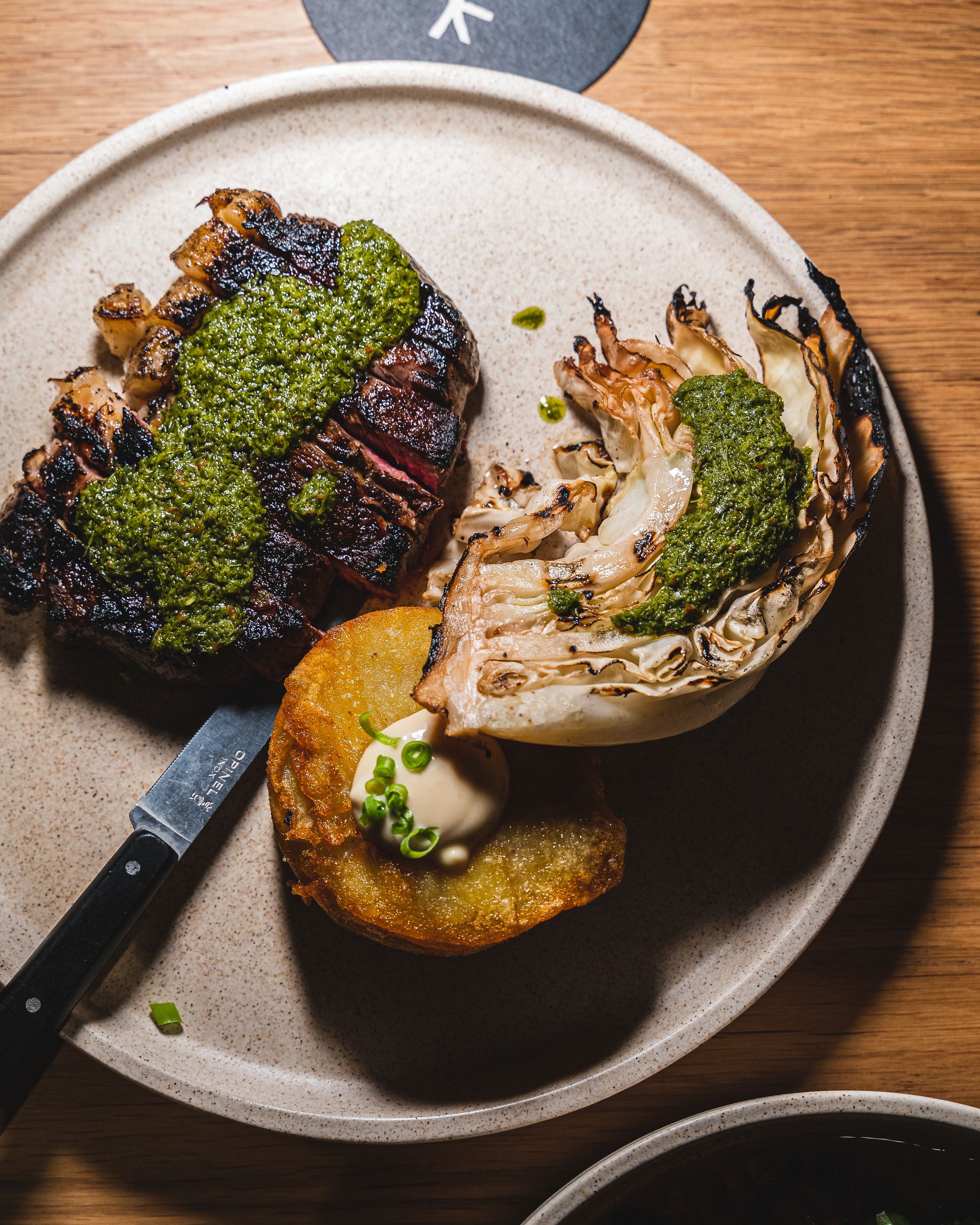 Close up of steak and cabbage with chimichuri and a potato cake with sauce on top