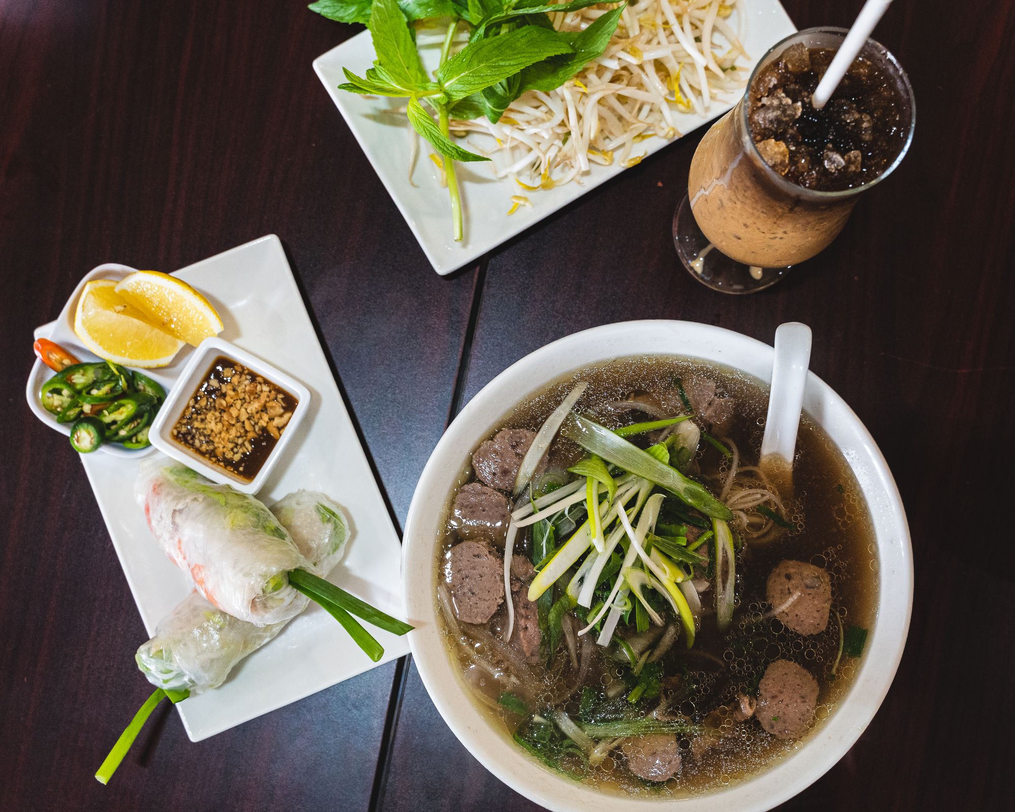 Birds eye shot of pho, Vietnamese iced coffee and a plate of rice paper rolls