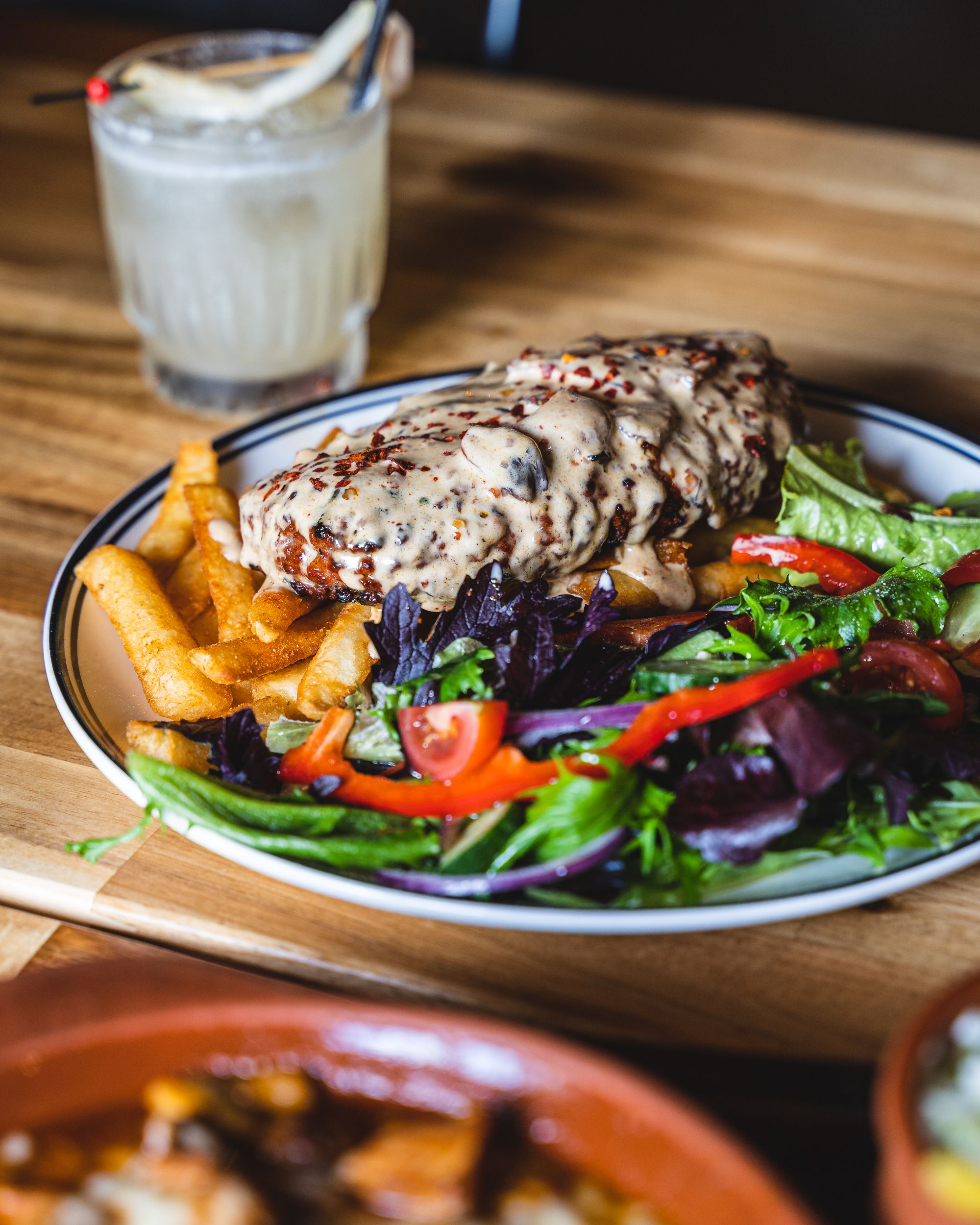 Close up view of a oval shaped beef patty with mushroom looking sauce, sitting on-top of chips and a salad