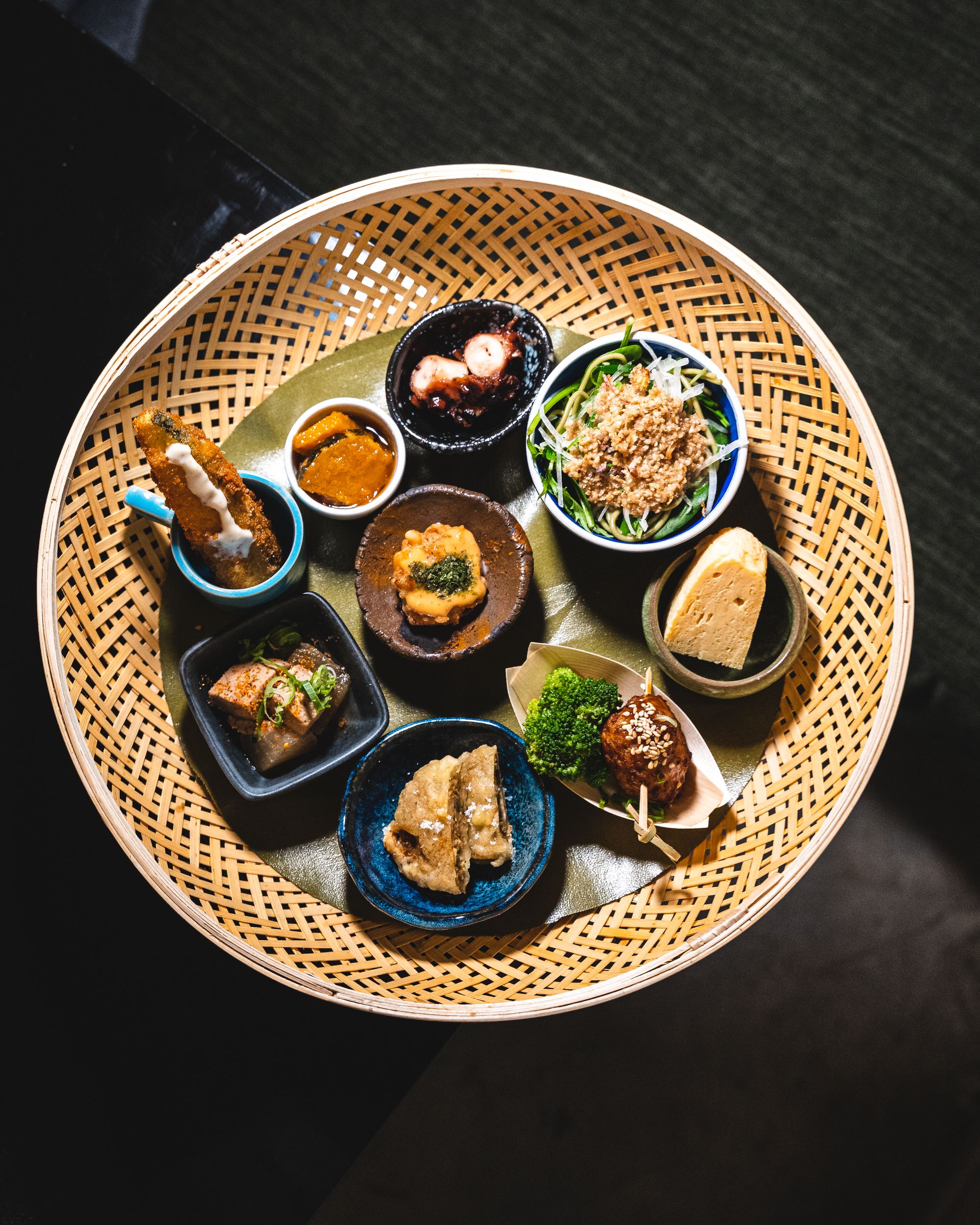 A circular basket with 9 different Japanese dishes 