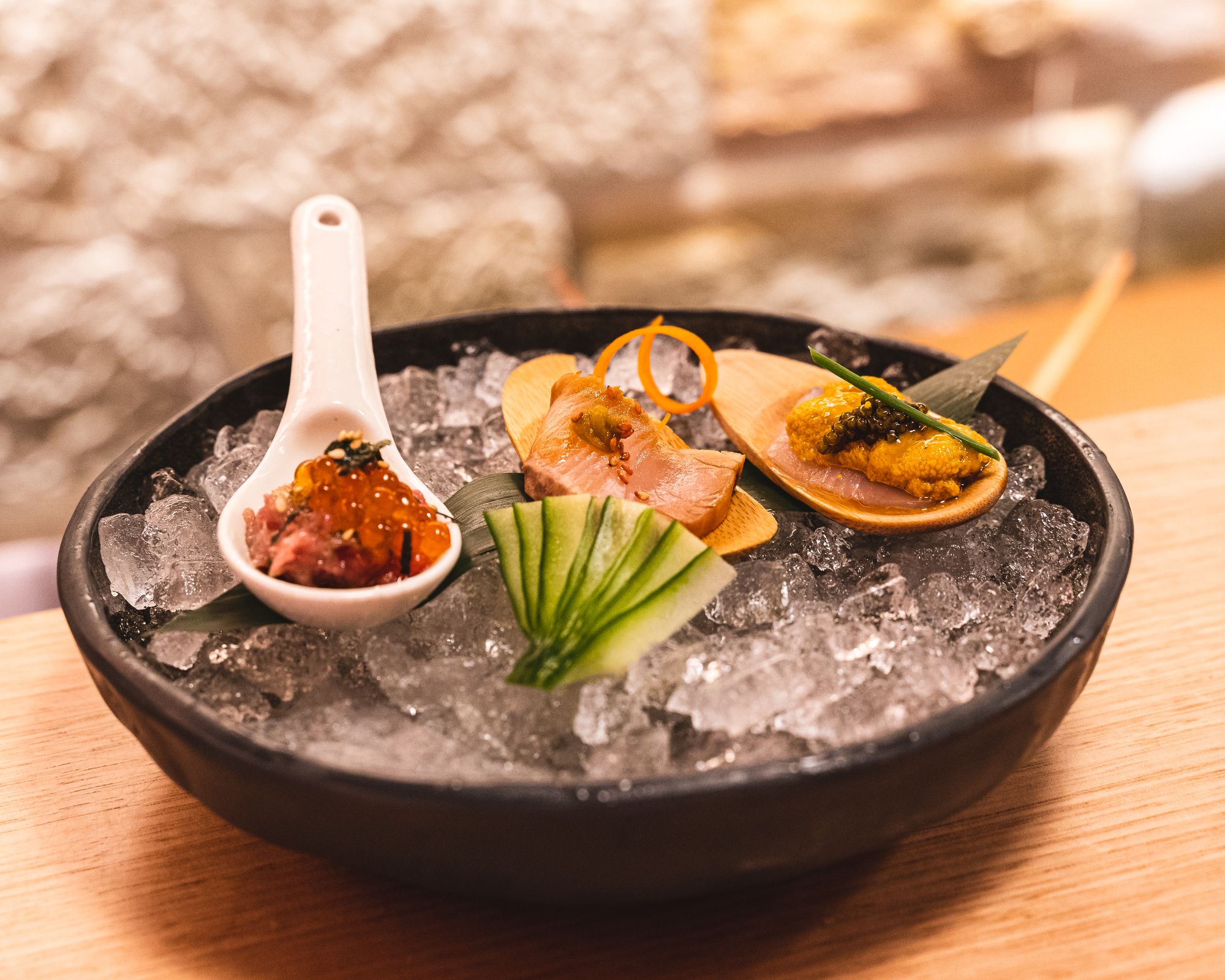 Round plate with ice and three different Japanese dishes - spoon with toro tartare, wooden paddle with sashimi and wooden paddle with uni