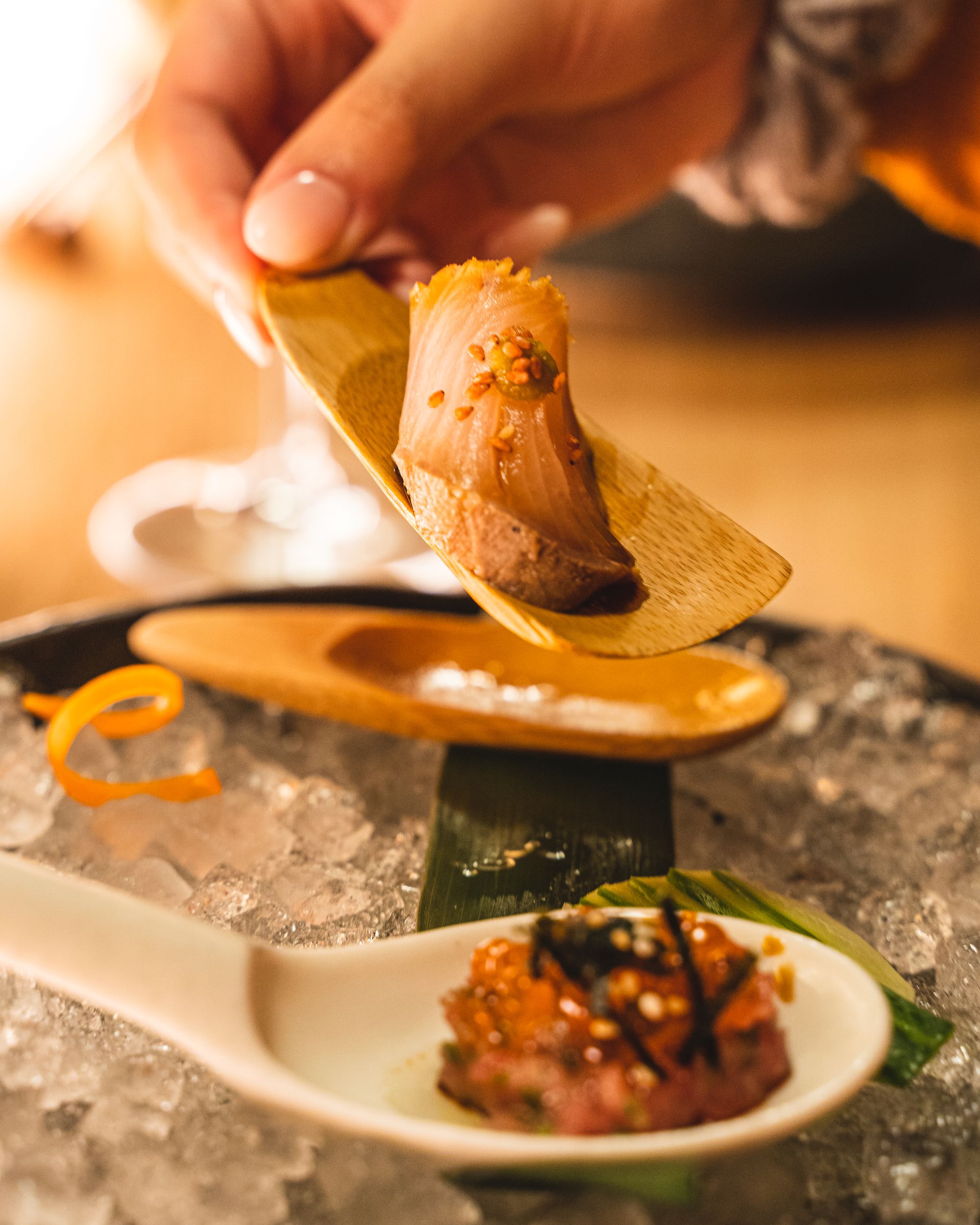 Fingers holding a small wooden paddle with yellowtail tataki