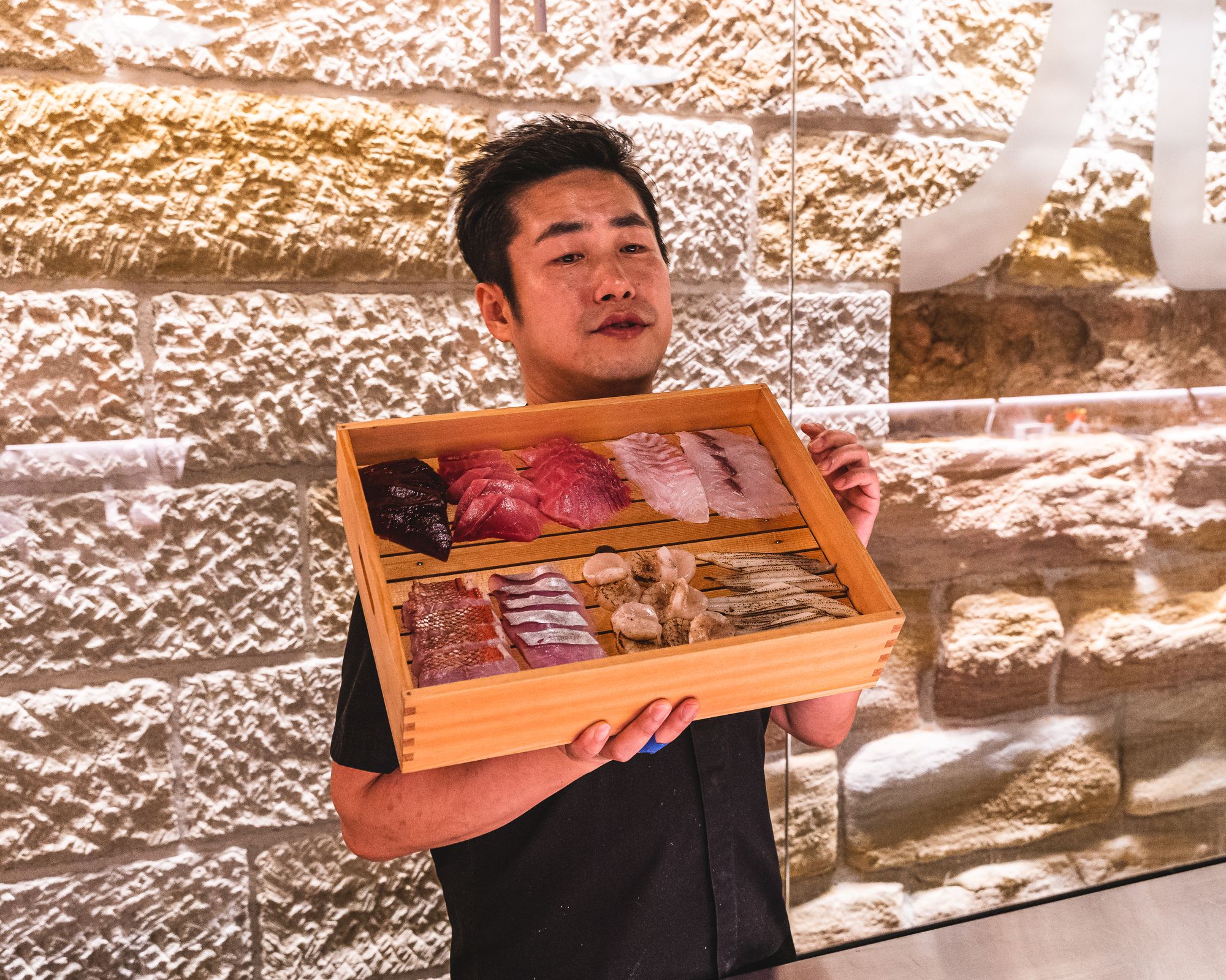 Asian chef holding a wooden box showcasing the produce for the evening