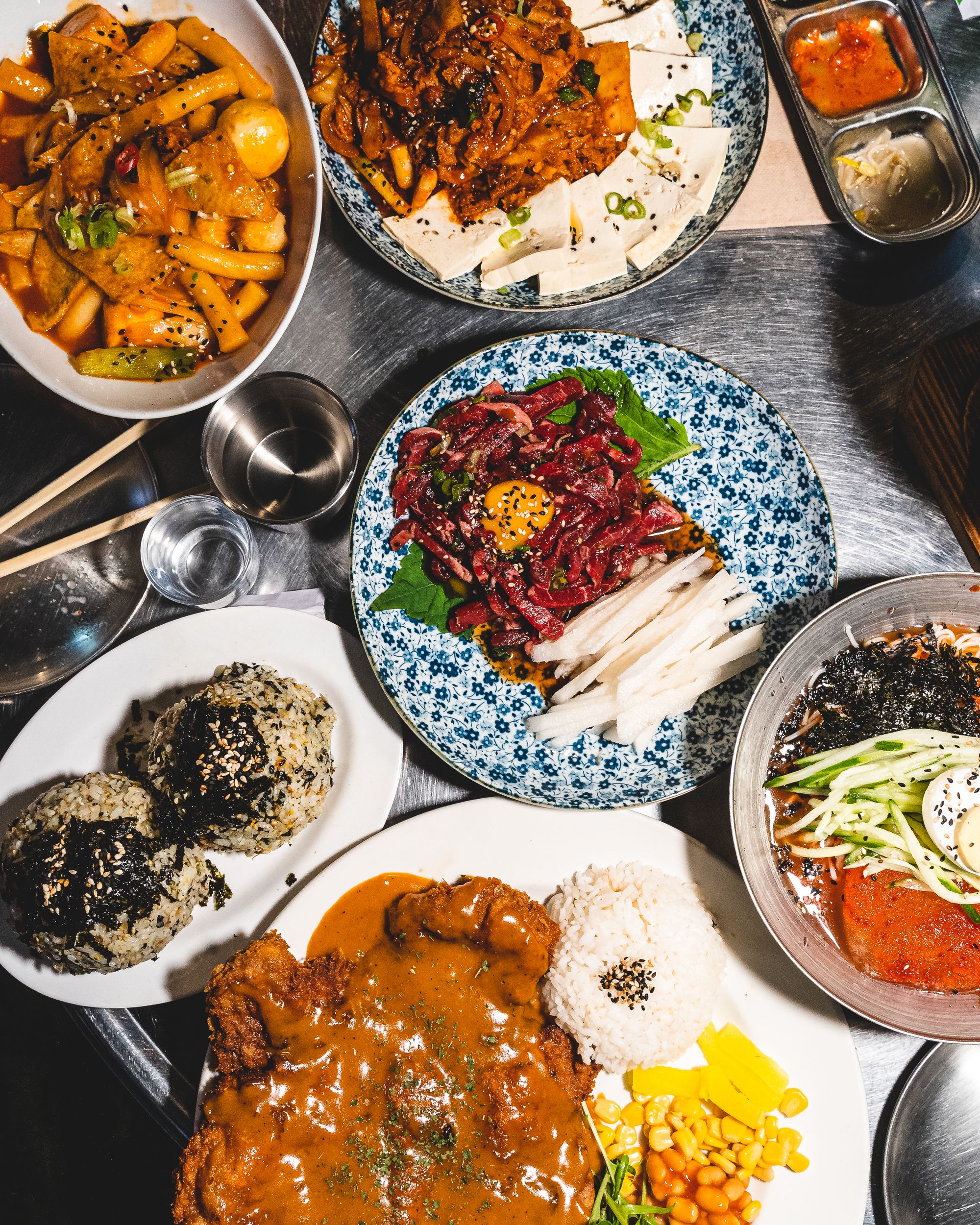 Top down shot showing a variety of Korean dishes on-top of a stainless steel table