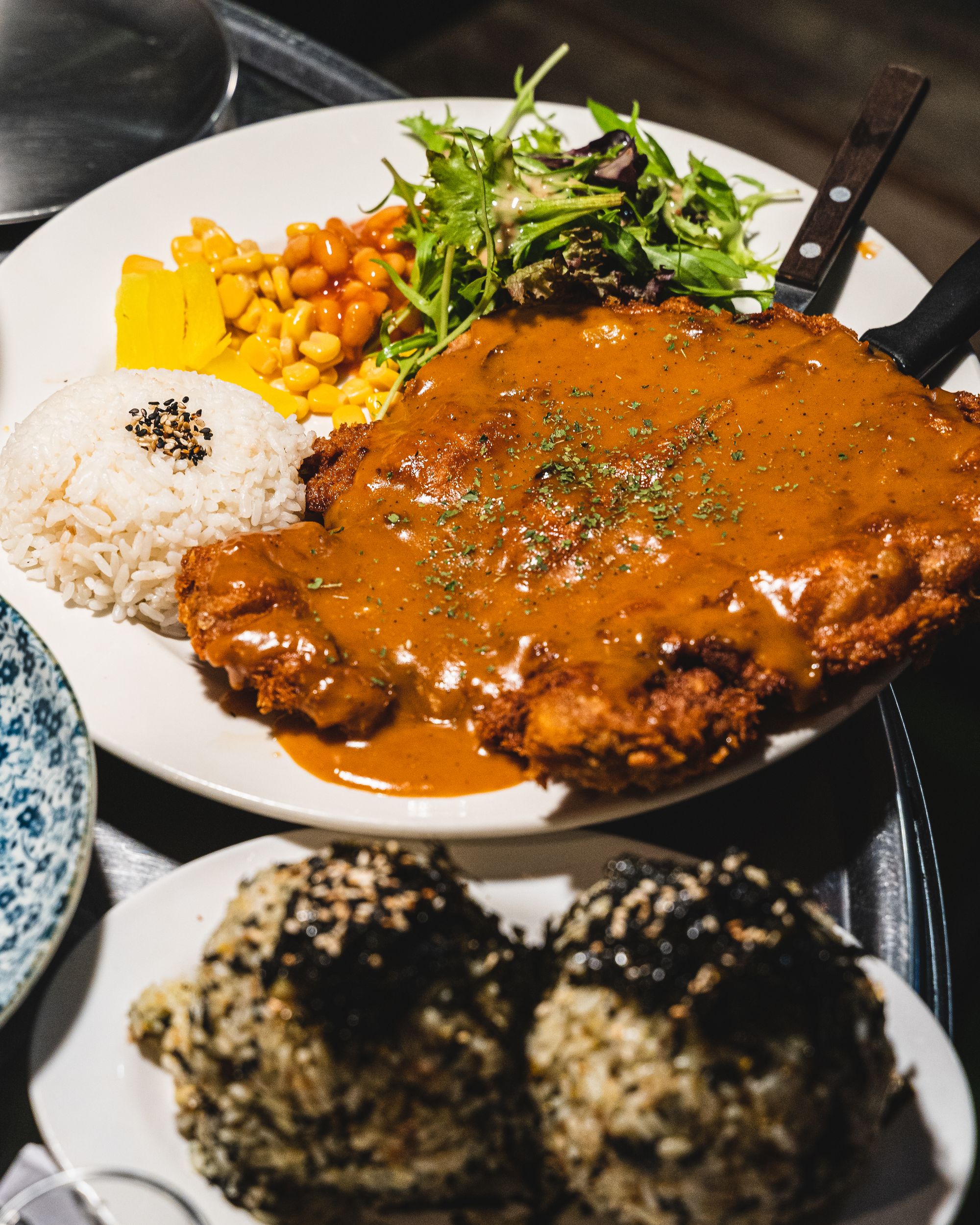 A large Korean donkatsu with rice, green vegetables, corn and baked beans