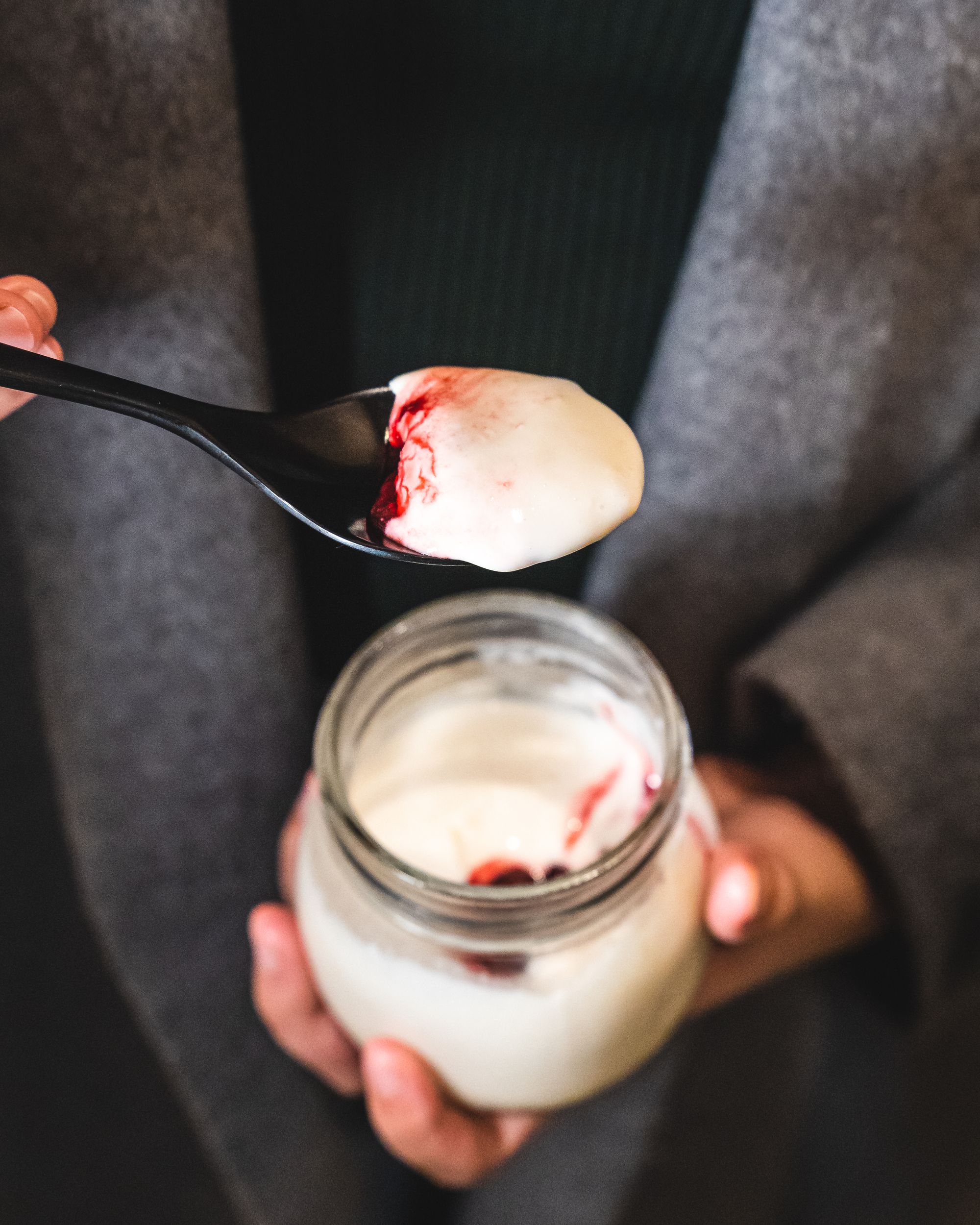 Hand holding a jar with cheesecake in it while another hand holes a spoonful of the cheesecake