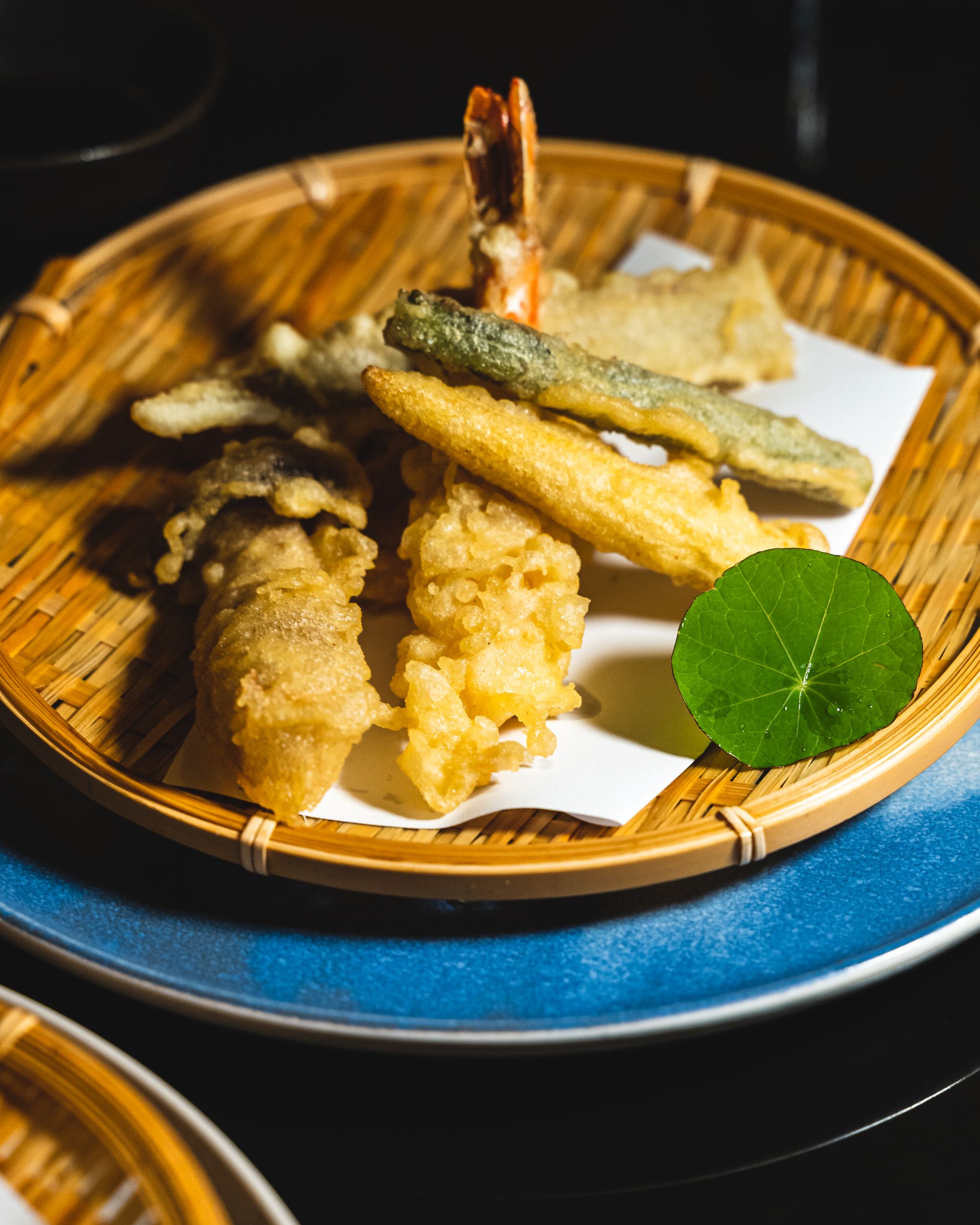 Assorted Japanese tempura on a basket on-top of a blue plate