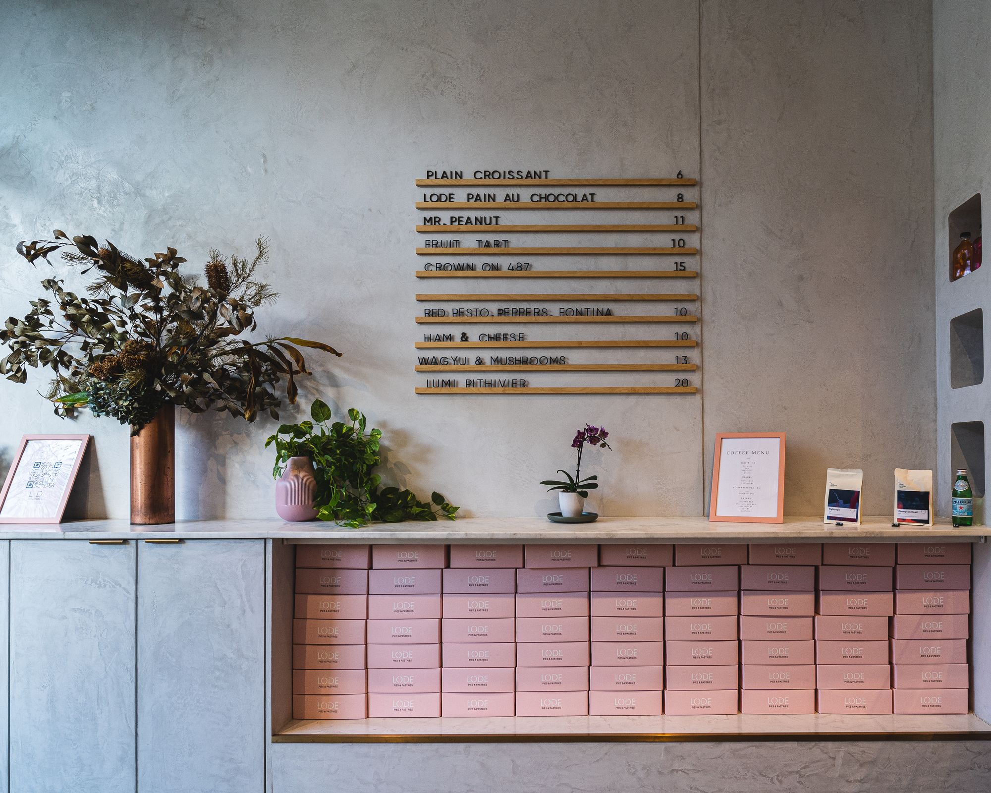 Interior shot of Lode Pies showing a menu on the wall, pink take-away boxes and flowers on a shelf