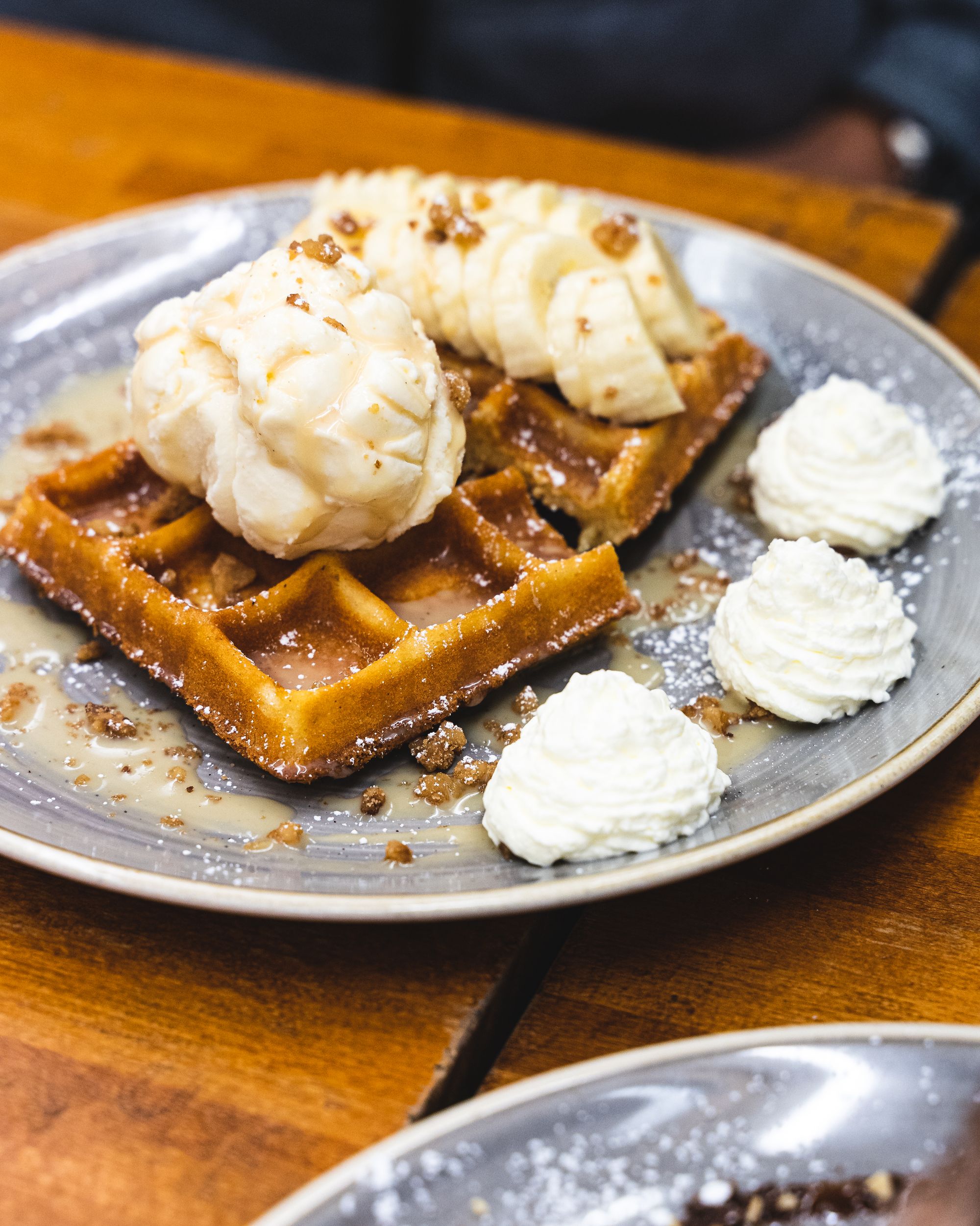 Close up of waffles with ice-cream, banana slices served with a side of whipped cream