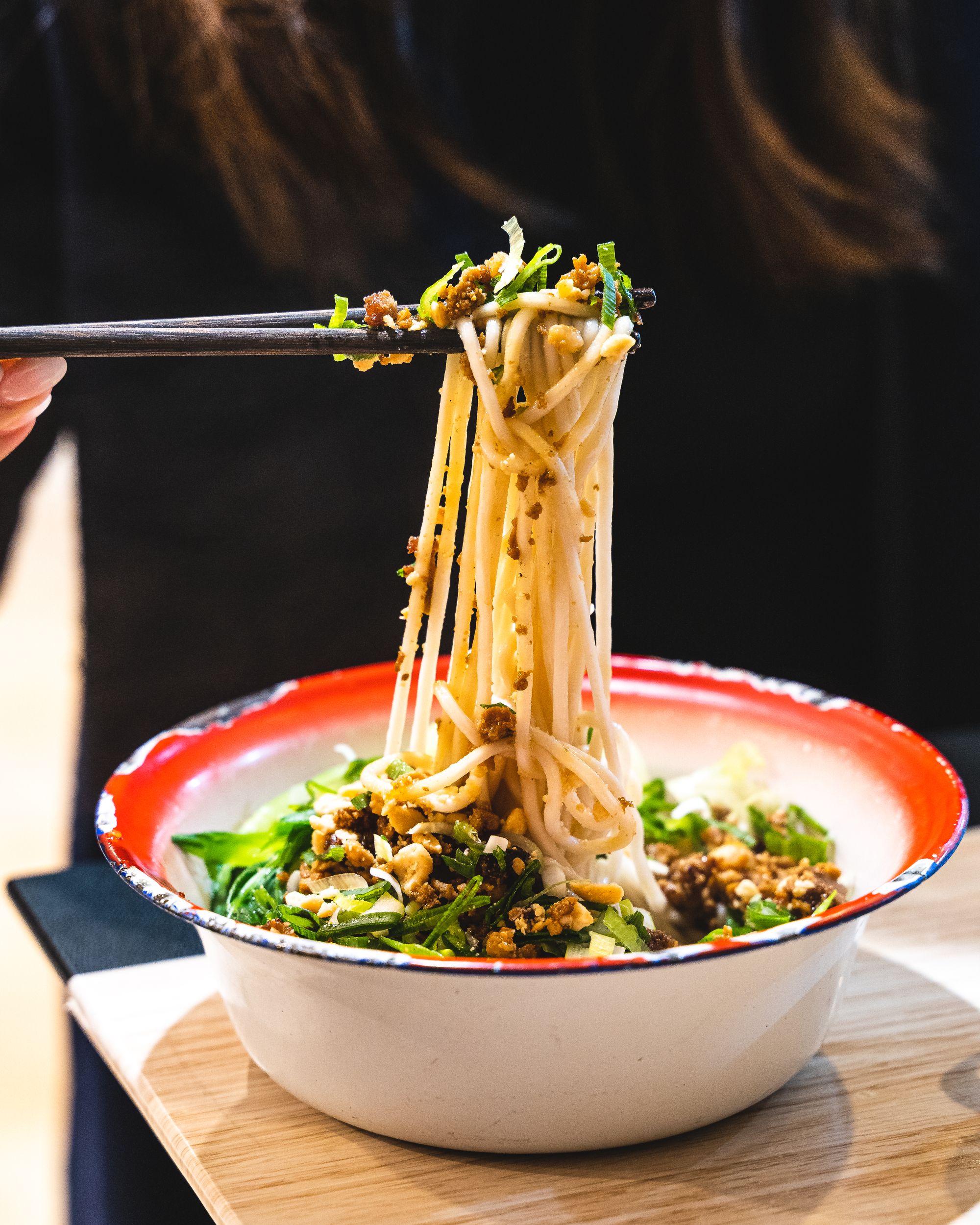 A bowl of noodles being lifted up by a pair of chopsticks