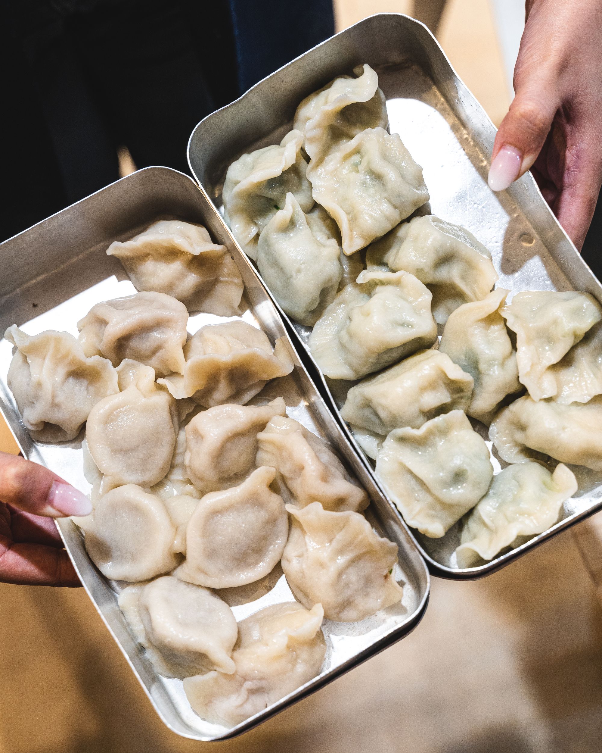 Manicured hands holding dumplings in two metal trays