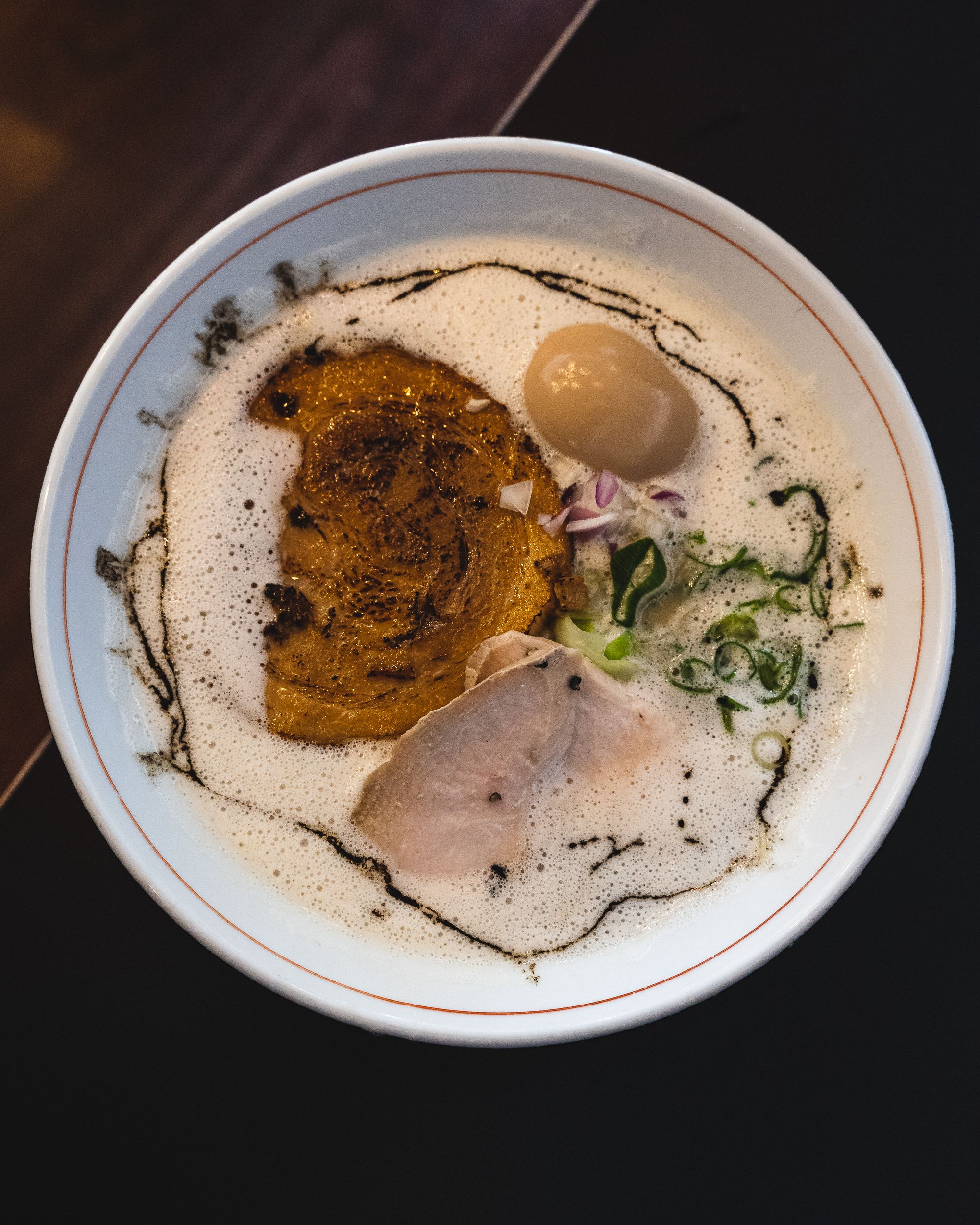 Overhead shot of frothy chicken broth ramen with pork and chicken chashu and and egg showing