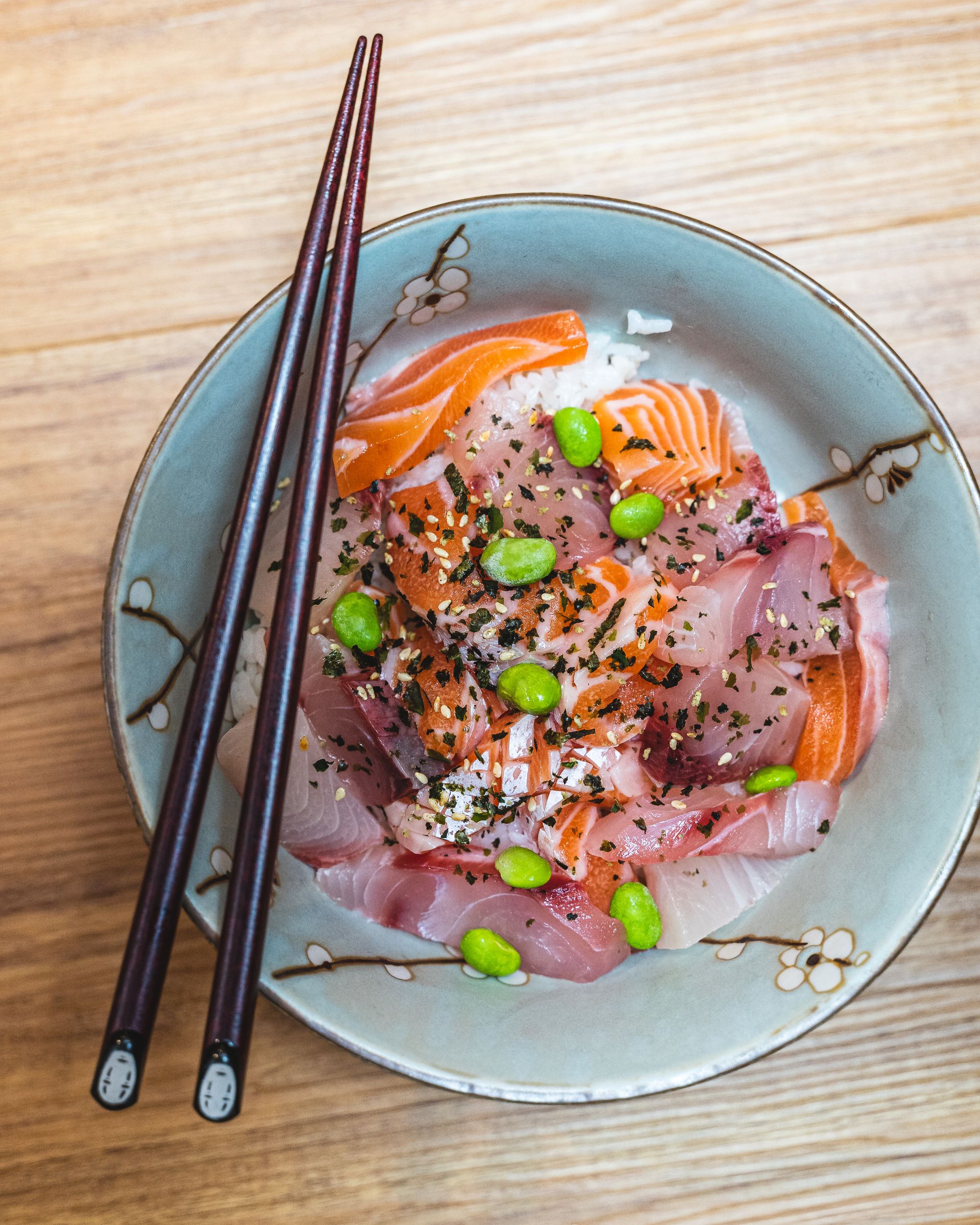 Close up of a chirashi bowl with chopsticks resting on-top