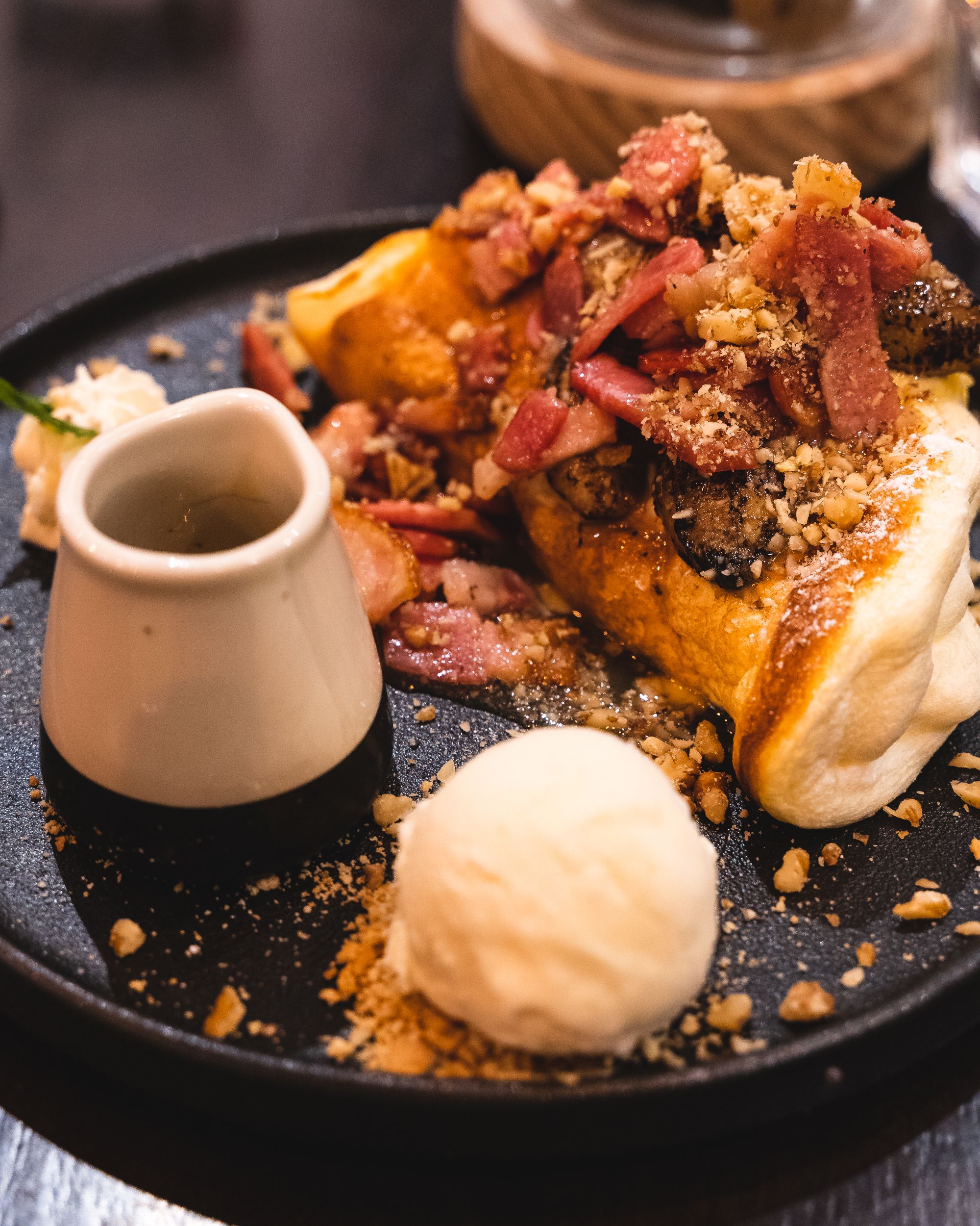 Plate with souffle pancakes topped with caramelised banana and bacon, with a side of ice-cream and honey