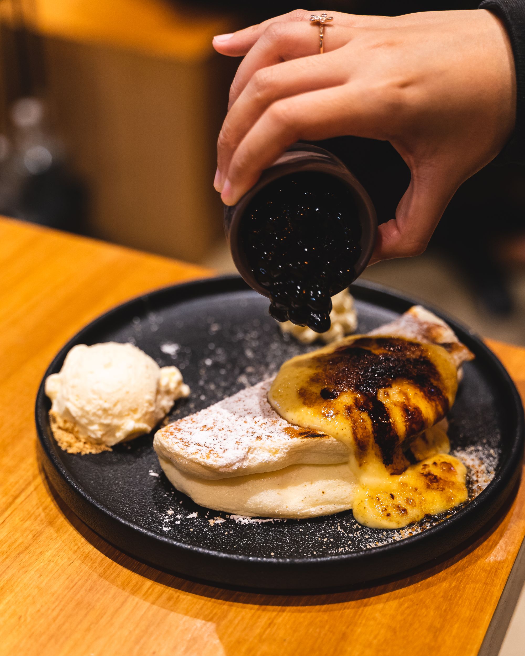 Hand pouring boba onto a souffle pancake on a plate with a side of ice-cream