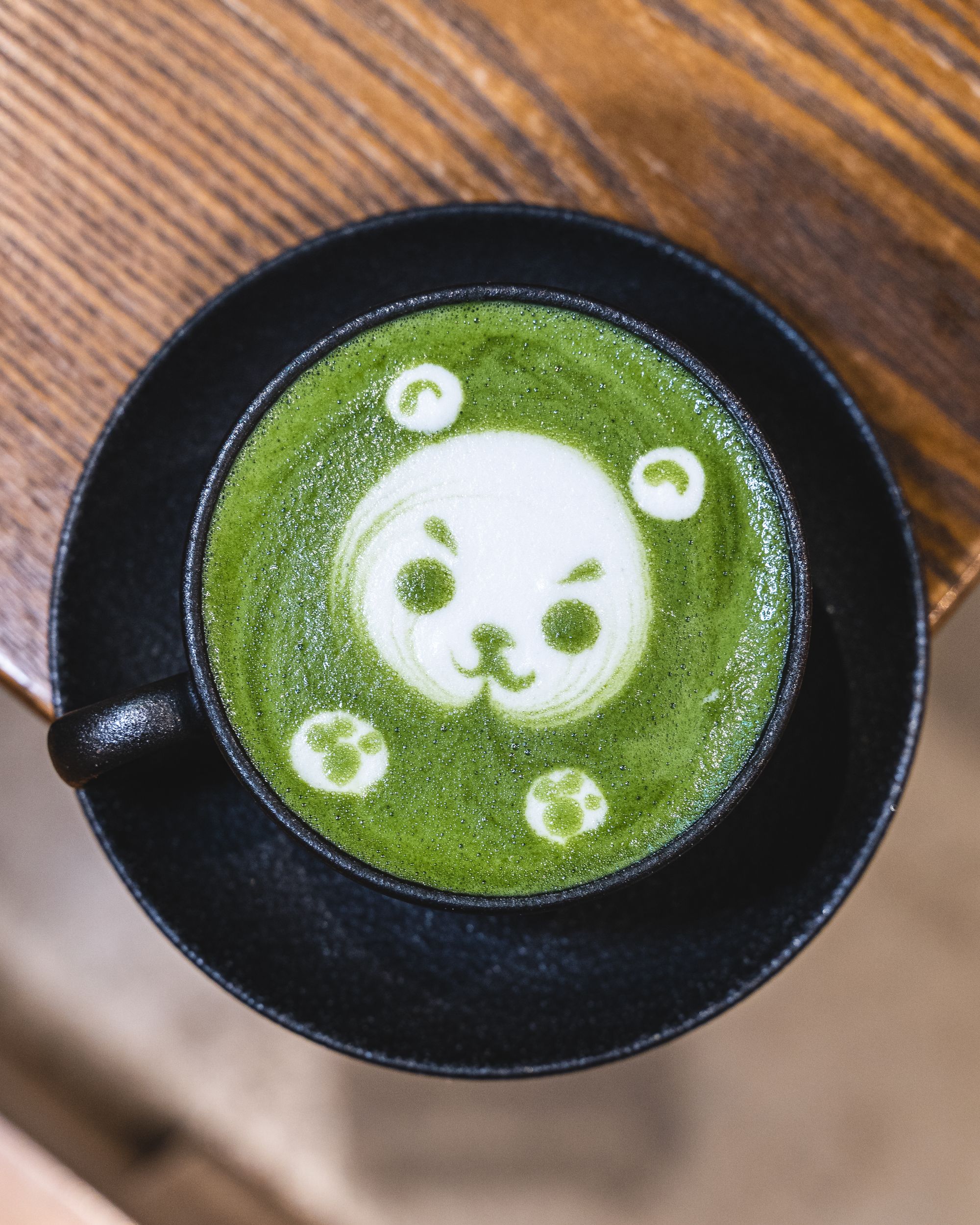 Matcha latte with cute teddy bear latte art, in a black mug and on a black plate