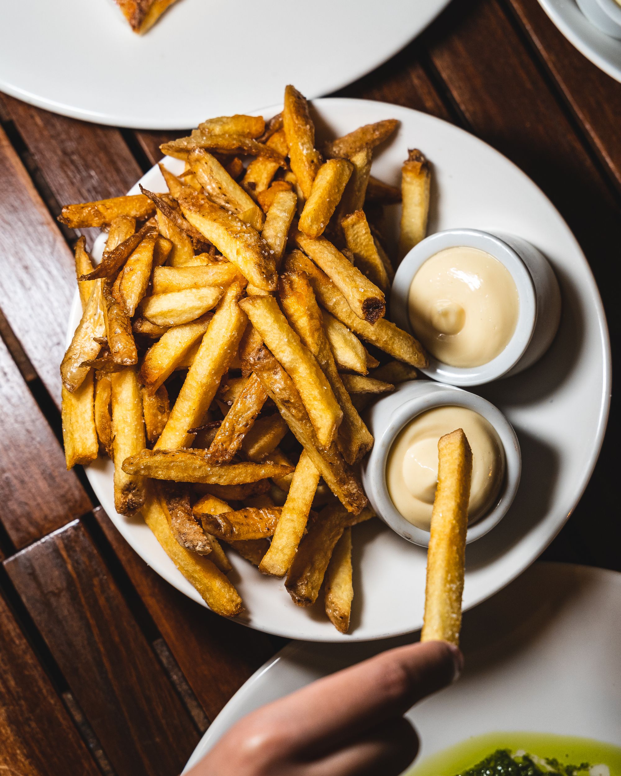 Close up of plate of fries with a hand dipping a fry into mayo