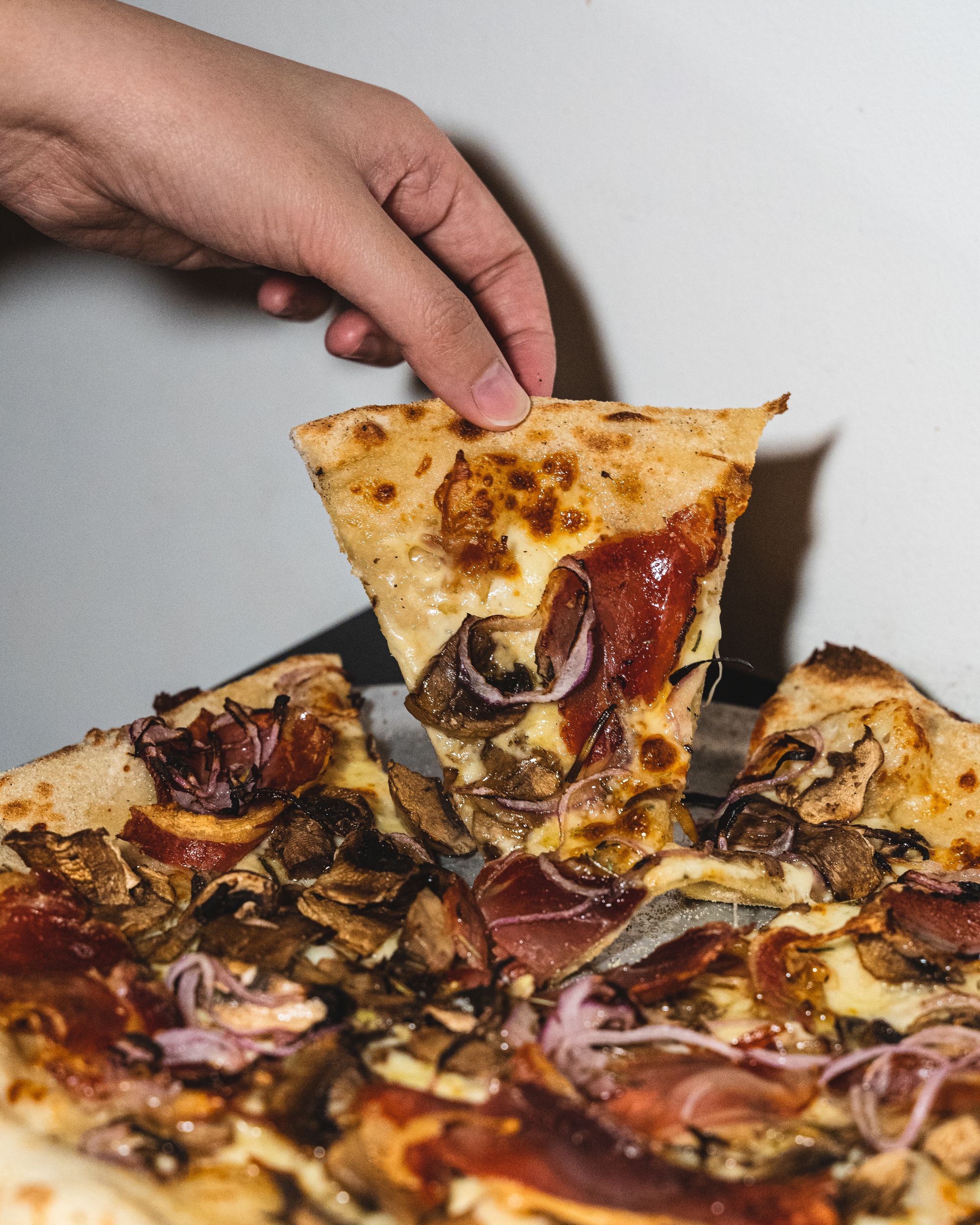 Close up of hand lifting up a single slice of pizza