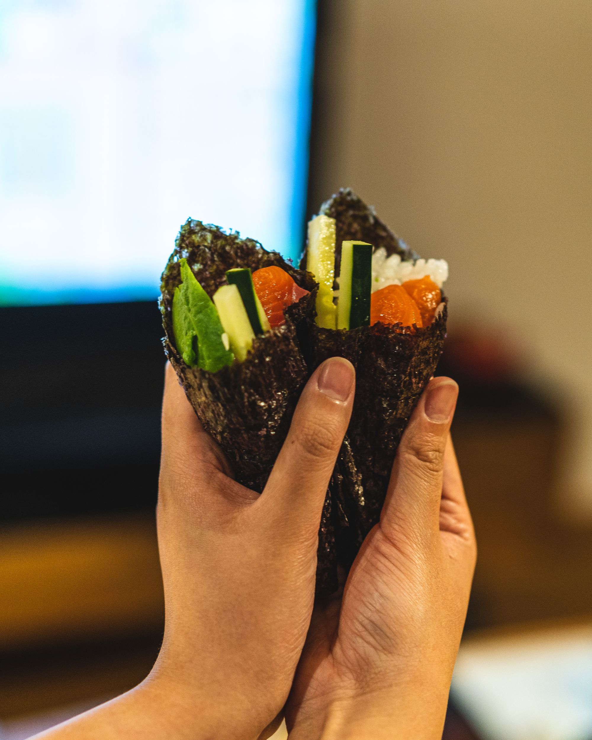 Two handroll sushi being held in hands