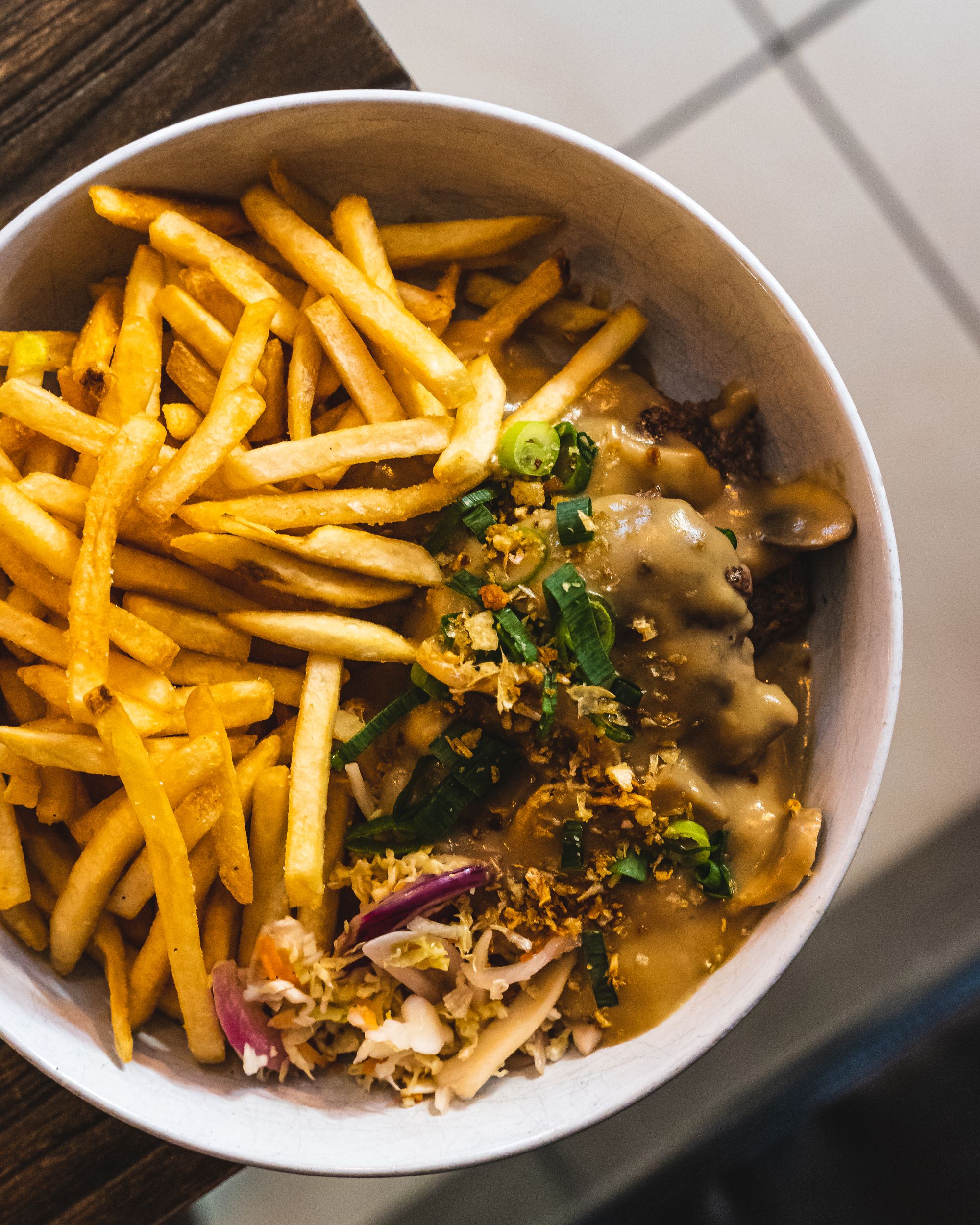 Top down of bowl with fries and hamburger patties covered with mushroom sauce