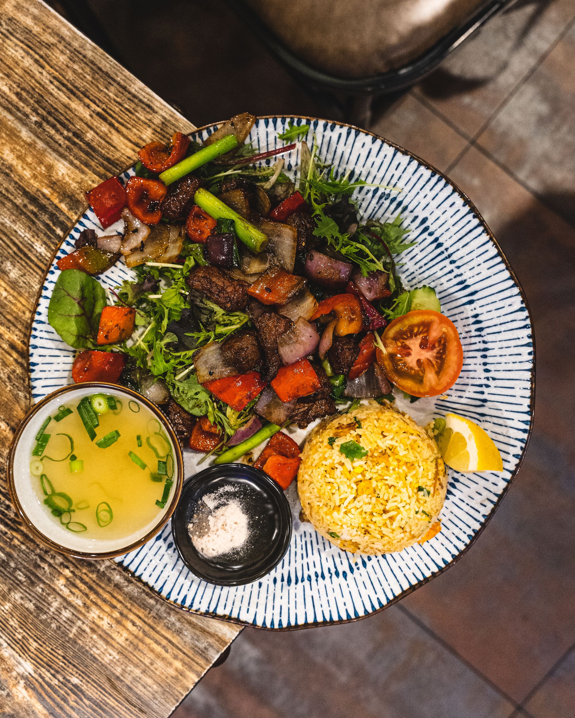 Top down shot of a palte with fried rice, stir fried beef and vegatables, a bowl of soup and a slice of lemon