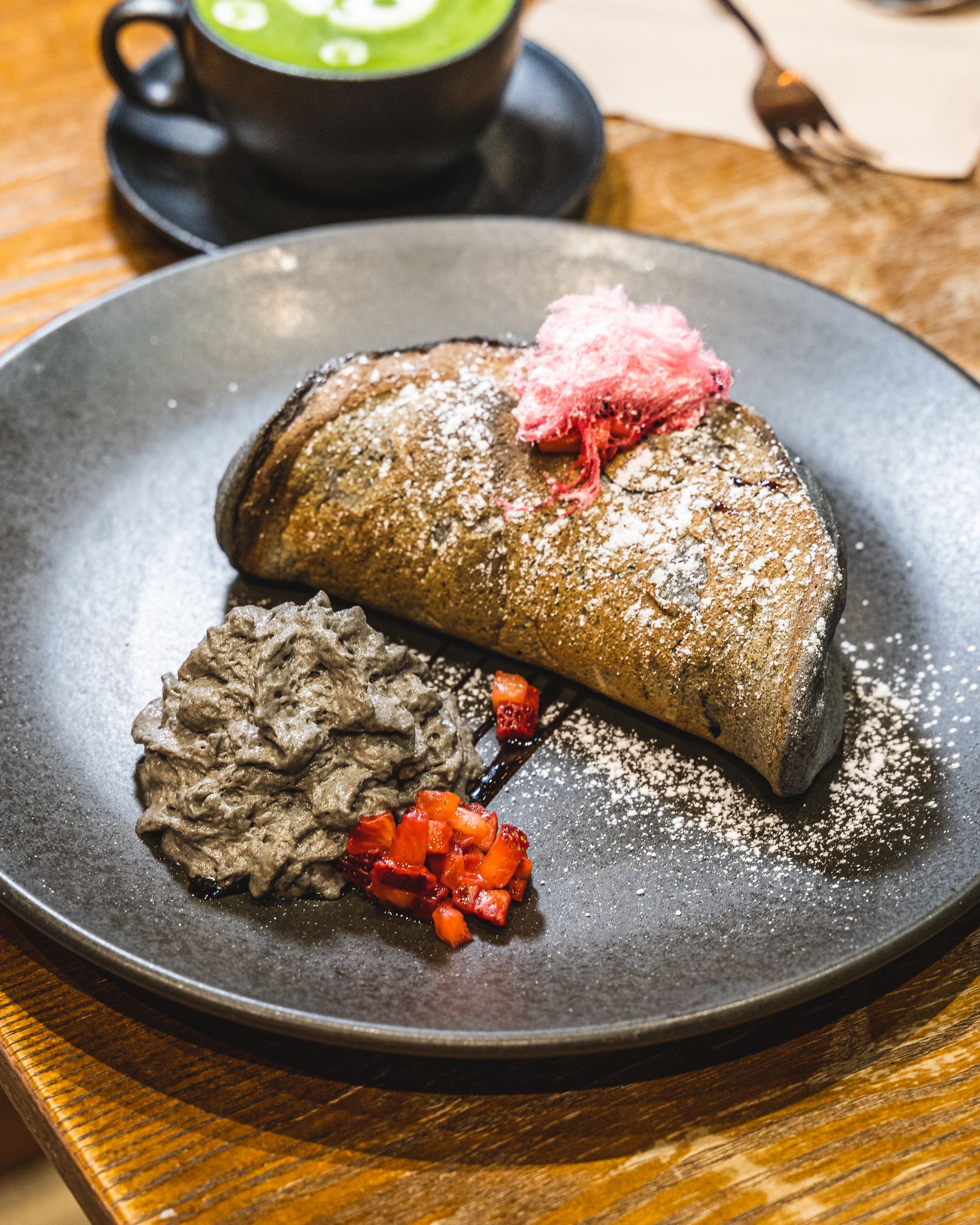 Close up of charcoal coloured fluffy pancake, with black sesame coloured cream cheese and diced strawberry